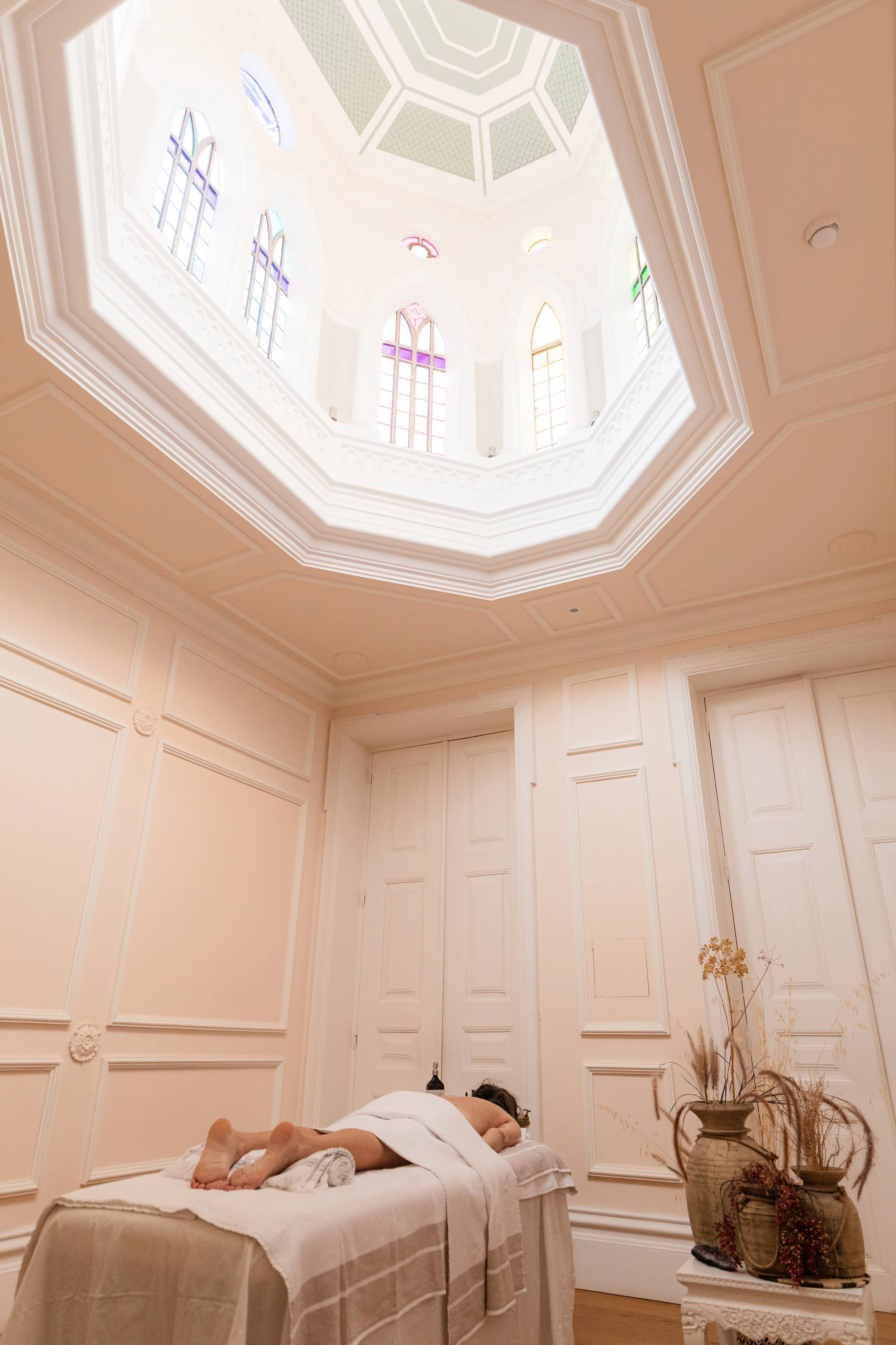 A guest receiving a La-Eva oil massage on a draped treatment table beneath the stained-glass octagonal cupola of the meditation room at Casa Fuzetta in Olhão.