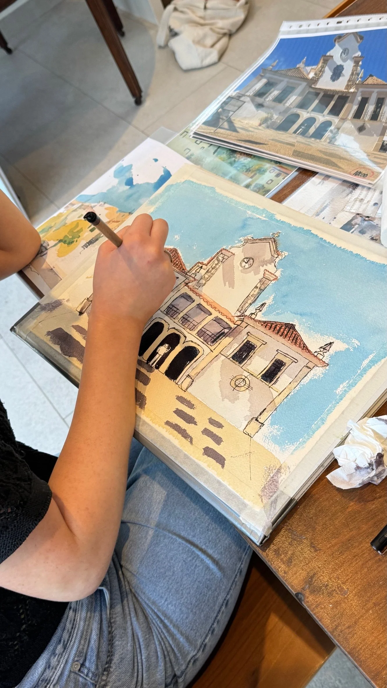 A watercolour sketching workshop in Olhão, close to Casa Fuzetta; a visitor paints the arched facade and clock tower of Olhão's Igreja Matriz, working from a reference photo.