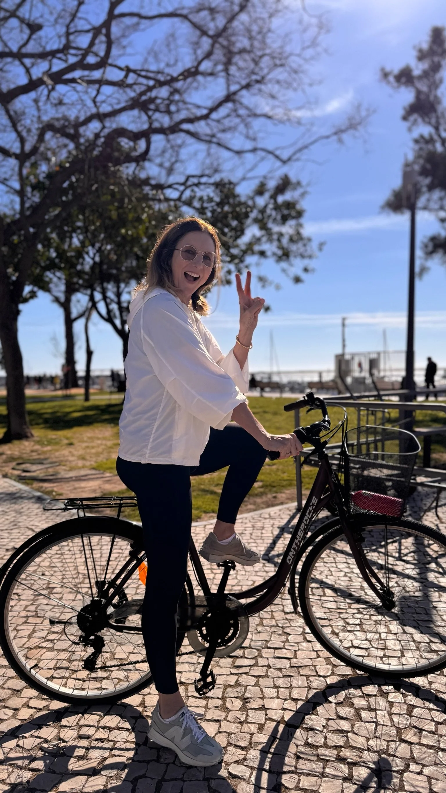 A visitor pauses on a rental bike on the Portuguese hand-cut calçada cobblestones by the Ria Formosa waterfront in Olhão, close to Casa Fuzetta, with sailboats moored in the marina beyond.
