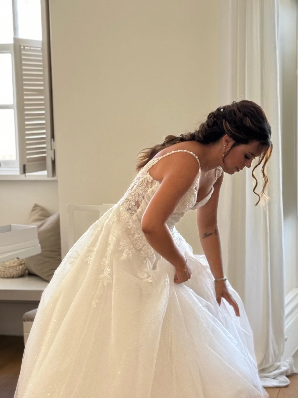 Casa Fuzetta House Manager Claudia lifts the hem of her wedding gown in a bedroom at Casa Fuzetta in Olhão with wooden floors and shuttered windows.