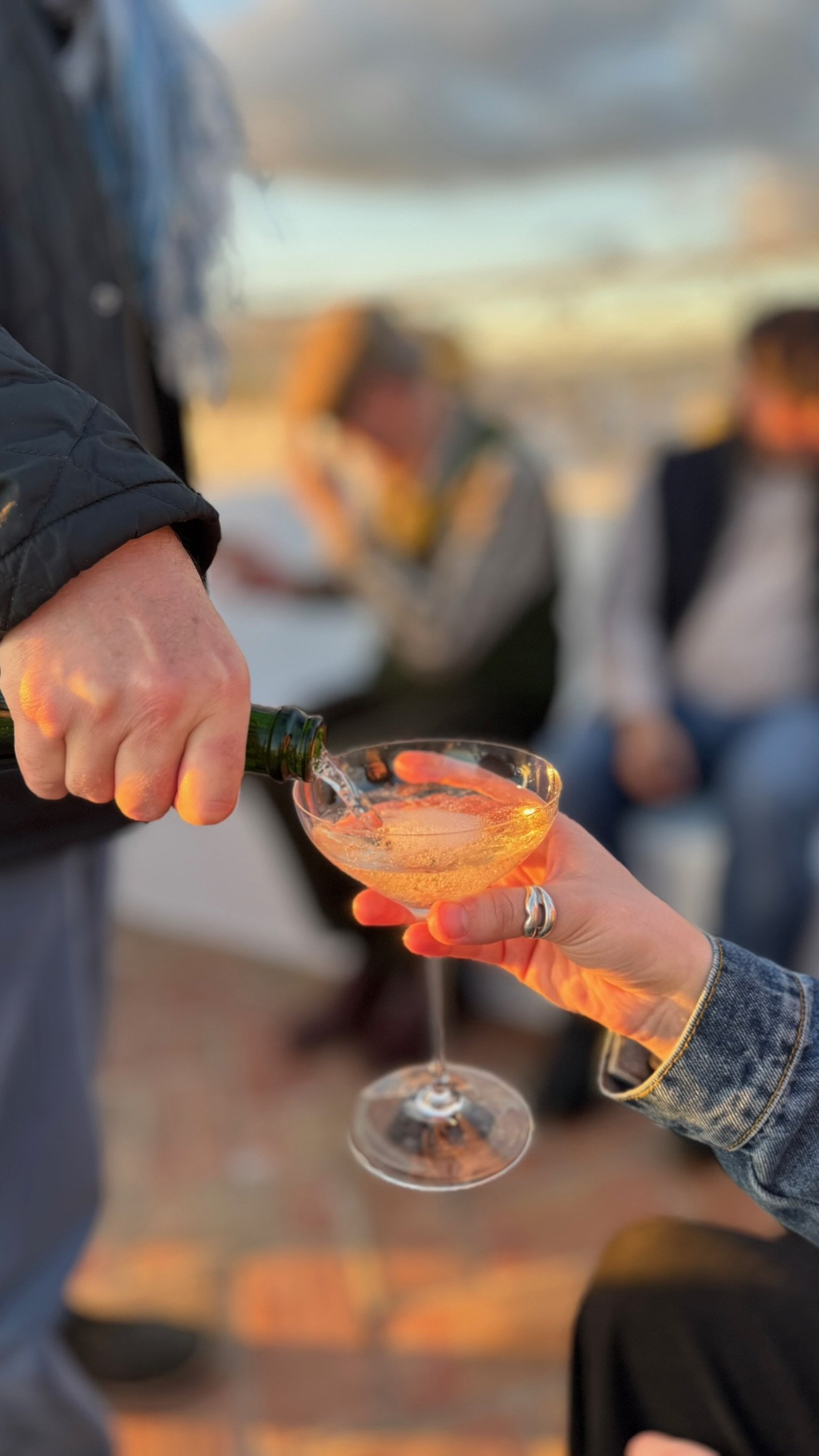 Champagne being poured into a coupe glass at sunset on the rooftop terrace at Casa Fuzetta, warm golden light catching the bubbles.