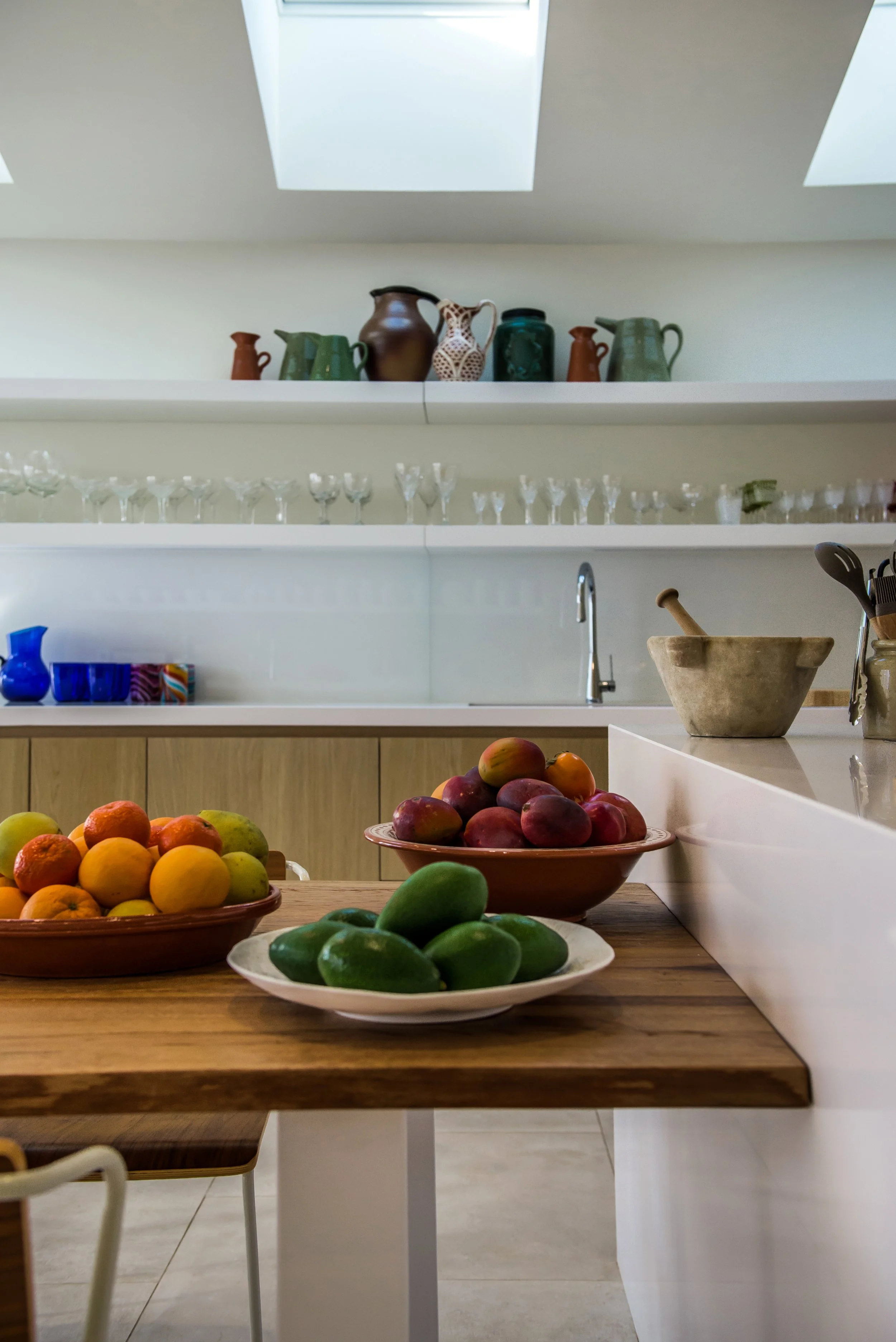 Inside the open-plan kitchen at Casa Fuzetta; skylights above shelves of ceramic pitchers and crystal wine glasses, with bowls of oranges, mangoes and avocados on the counter below.