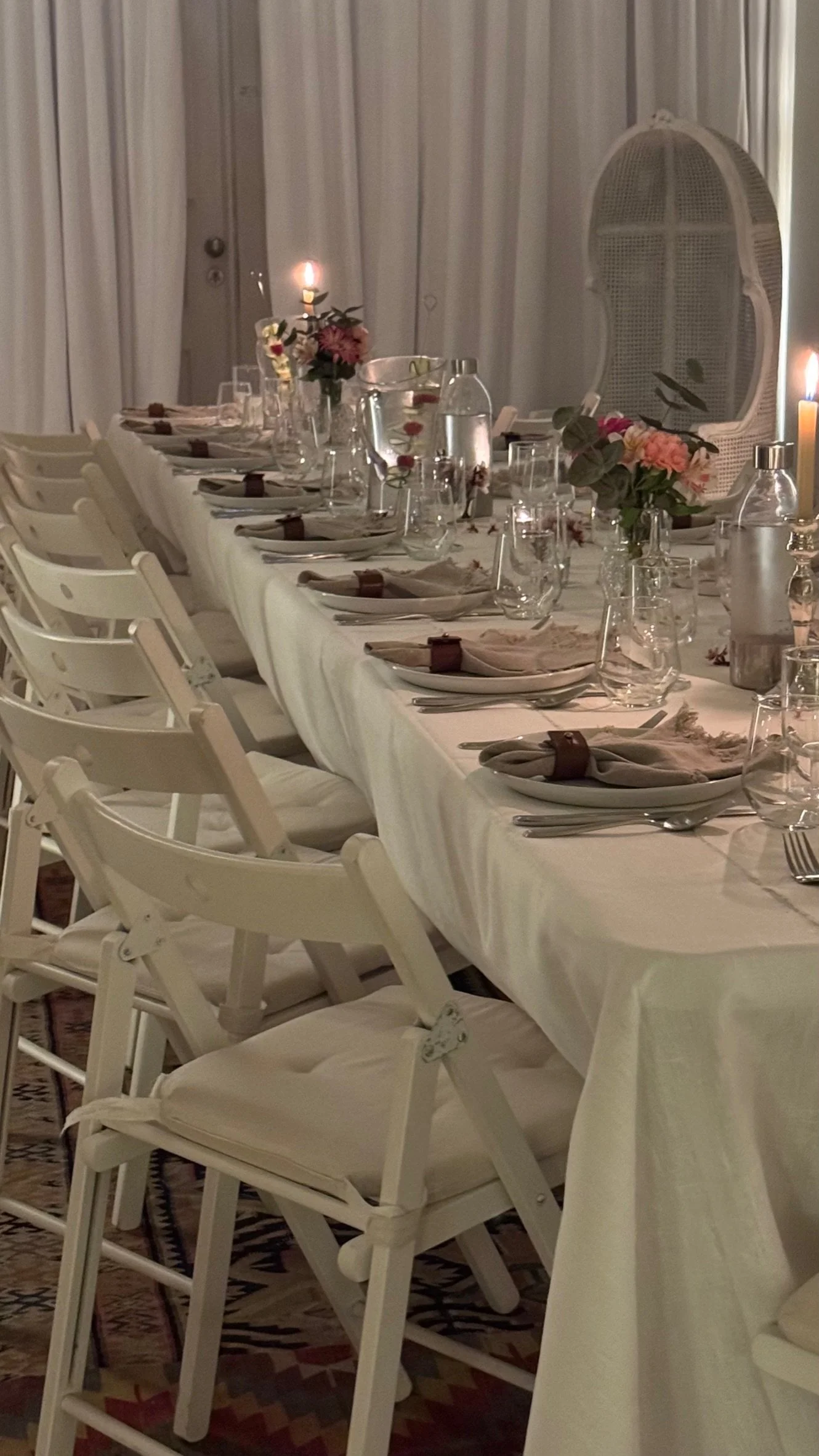A long dining table set for a candlelit dinner at Casa Fuzetta; white linen, tapered candles, small flower arrangements and a woven cane bishop's chair at the head.