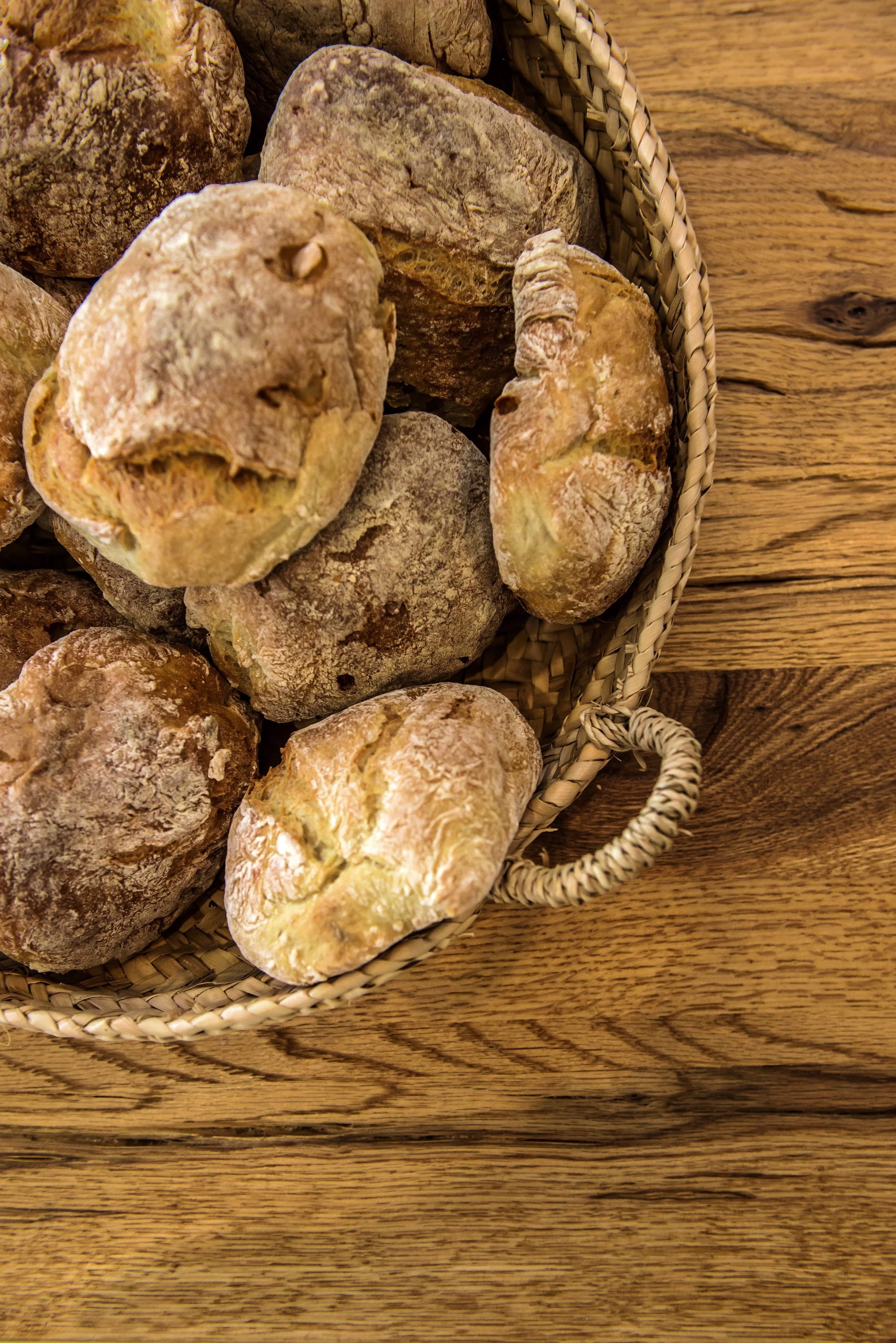 A woven basket of freshly baked Portuguese bread rolls on the rustic wooden kitchen table at Casa Fuzetta.
