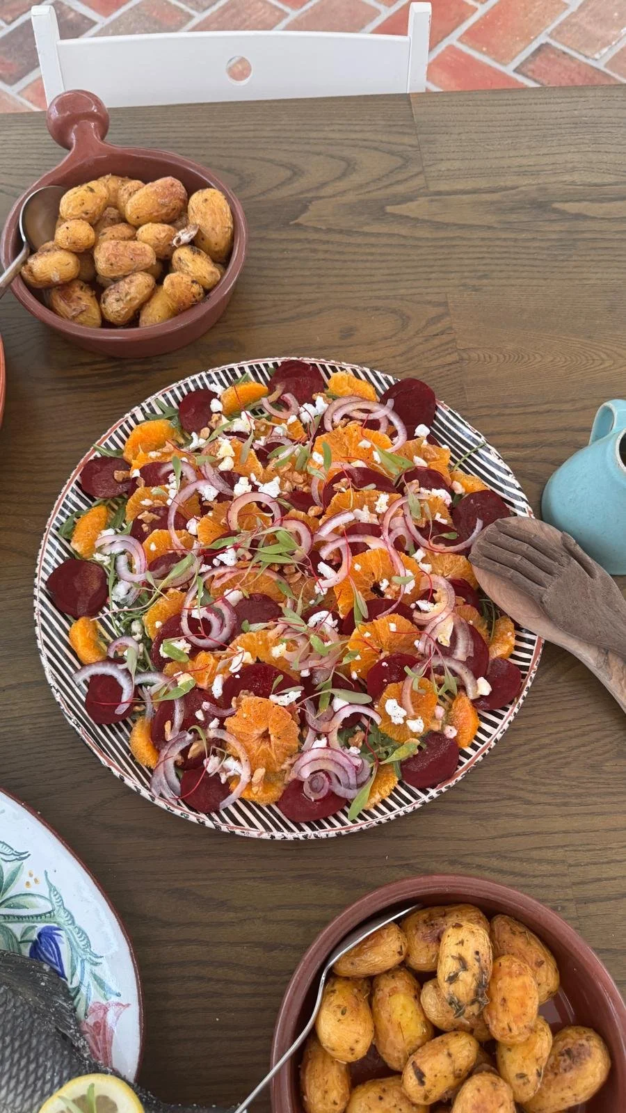 A beetroot and orange salad with red onion, feta and walnuts on a striped platter at Casa Fuzetta, beside a terracotta bowl of roasted new potatoes on the sunlit terrace table.