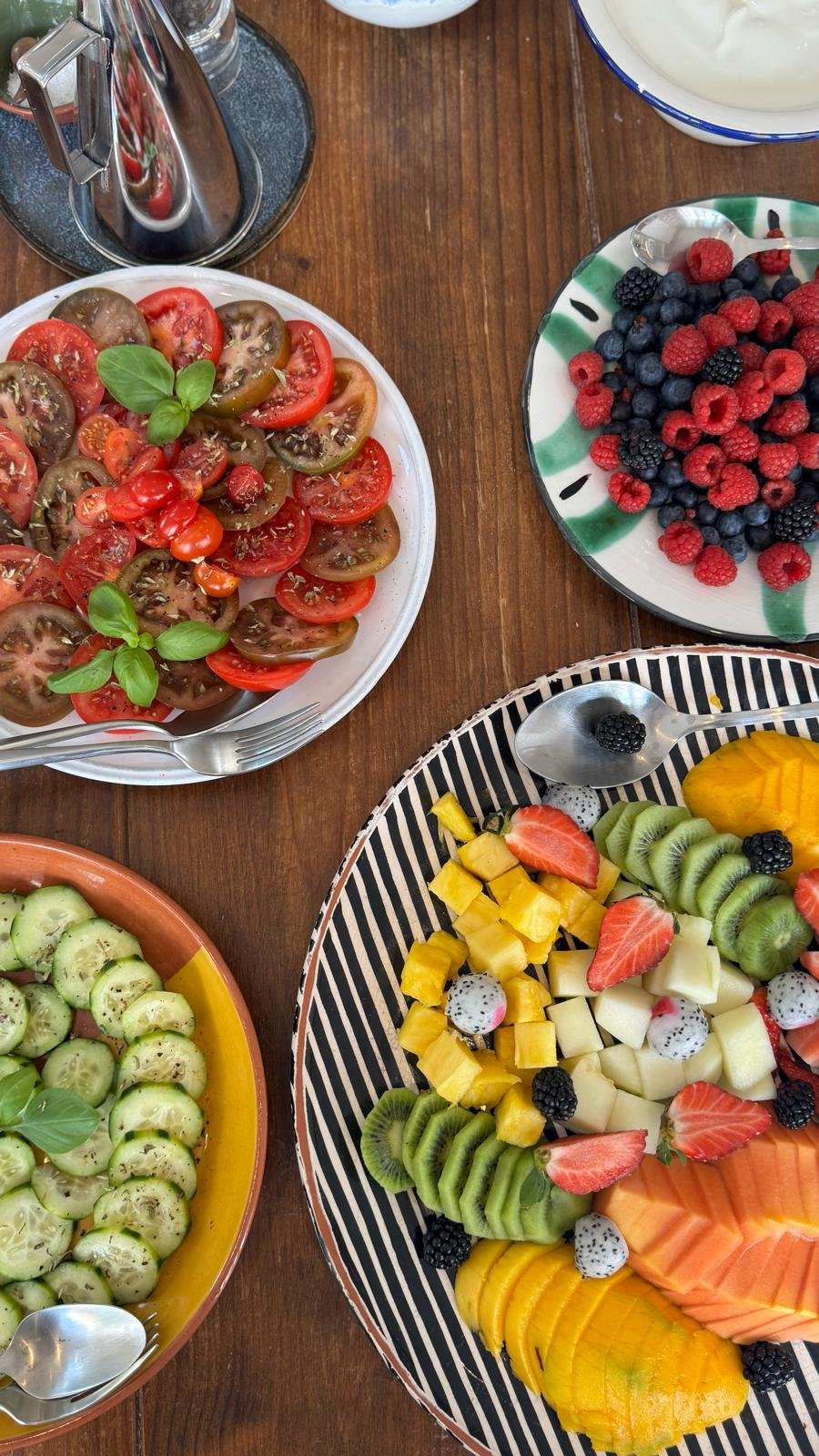 An overhead of the breakfast spread at Casa Fuzetta; heirloom tomatoes with basil, a bowl of berries, cucumber salad and a striped platter of pineapple, kiwi, papaya, mango and dragonfruit.