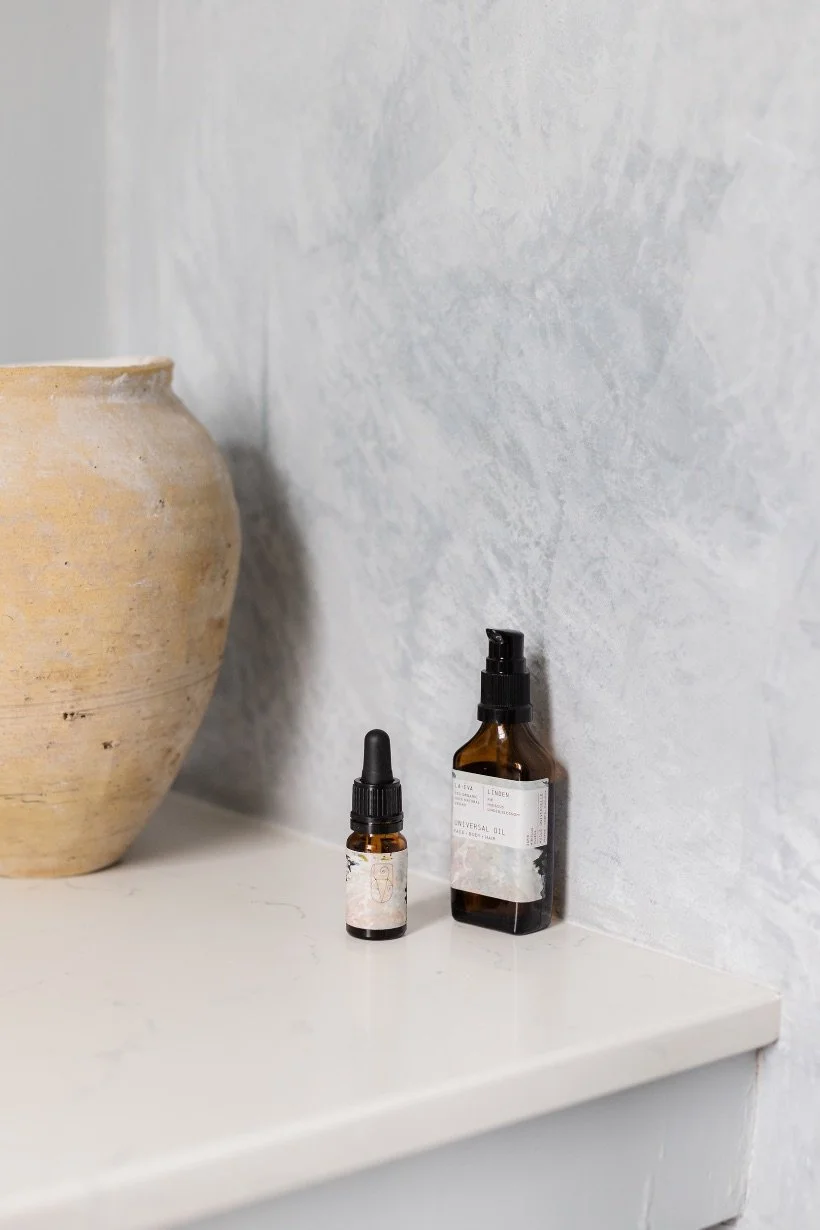 La-Eva Linden Universal Oil — a 15ml dropper bottle beside the 200ml pump bottle, on a stone shelf with a rustic terracotta pot