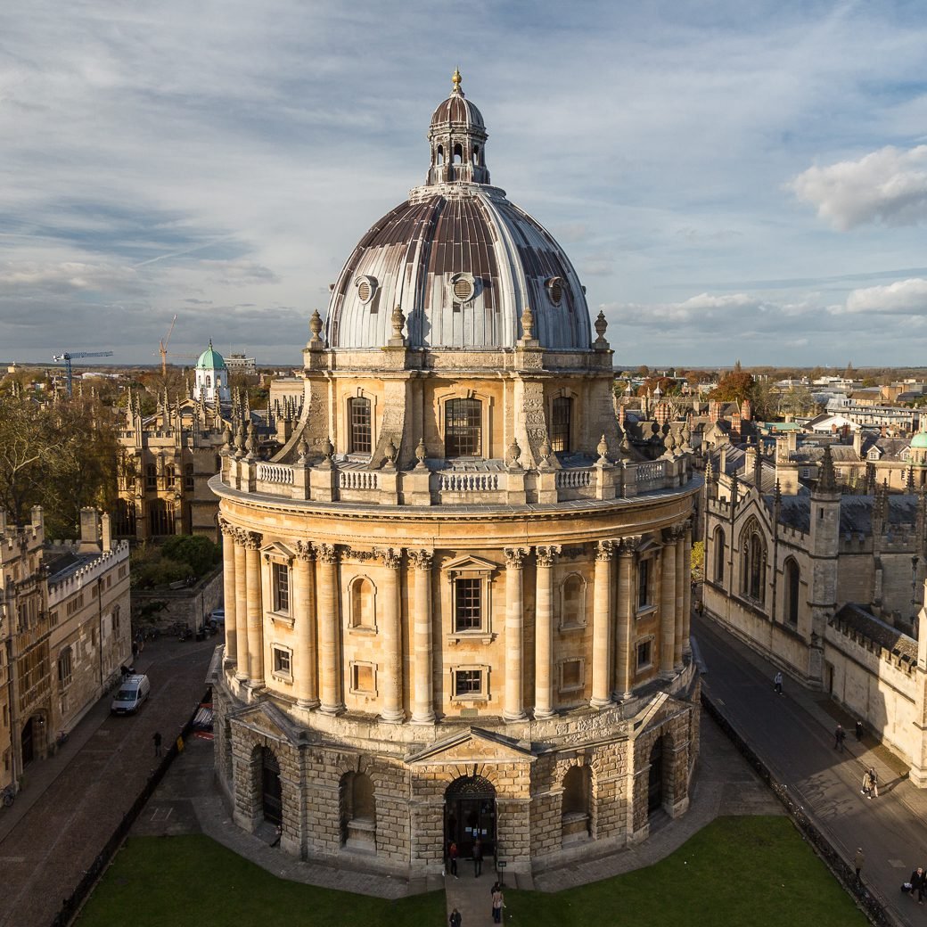 The Radcliffe Camera, a domed reading room of Oxford's Bodleian Libraries, seen from above on an autumn afternoon among the honey-coloured stone colleges of Radcliffe Square.