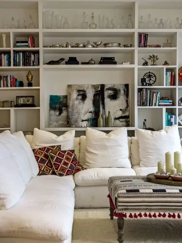 The library at Casa Fuzetta in Olhao: Meinke Flesseman's portrait panels set into white shelves of books, glass decanters and silver, above a linen sofa and a striped, tasselled ottoman.