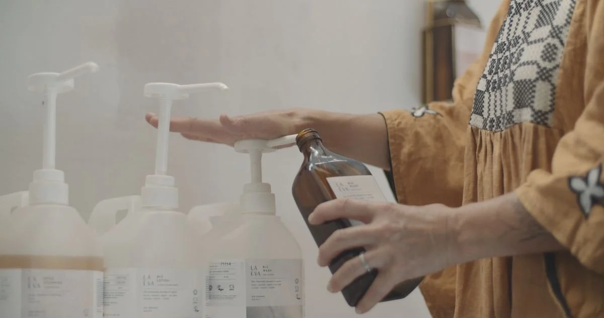 A woman refilling a La-Eva amber Blu wash bottle from large refill pumps, the closed-loop system that has kept refillable bottles in every Casa Fuzetta bathroom for a decade.