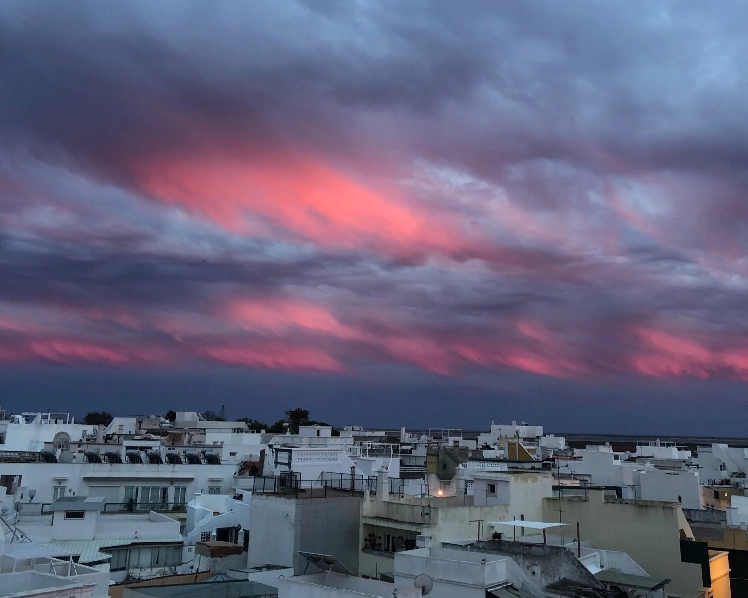 A pink-and-grey sunset sky over the whitewashed rooftops of Olhão, home to Casa Fuzetta, with the Ria Formosa lagoon visible on the horizon.
