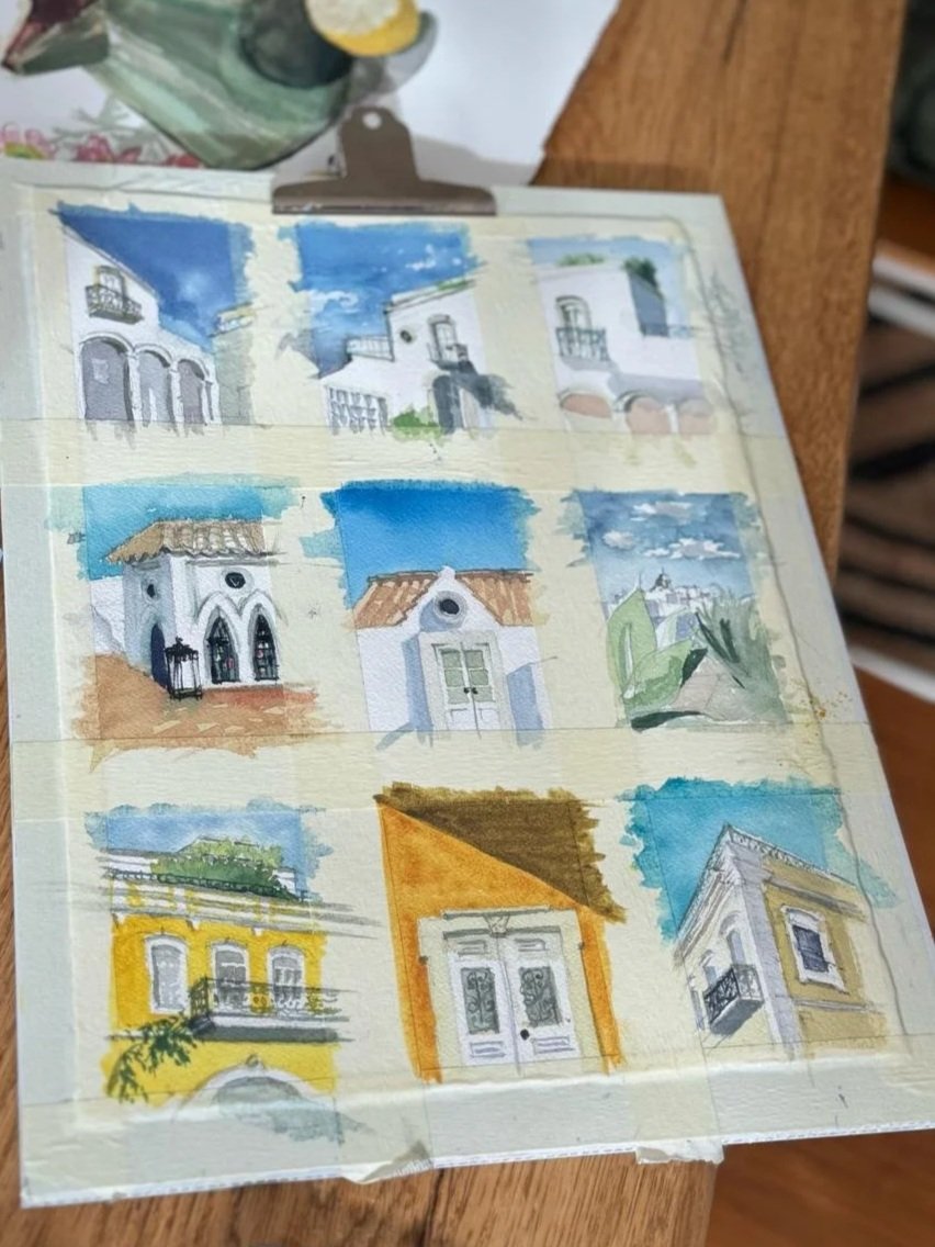 A page of nine small watercolour studies of Olhao architecture; white and yellow facades, balconies, chimneys and the Gothic pavilion; masking-taped on a wooden table at Casa Fuzetta.