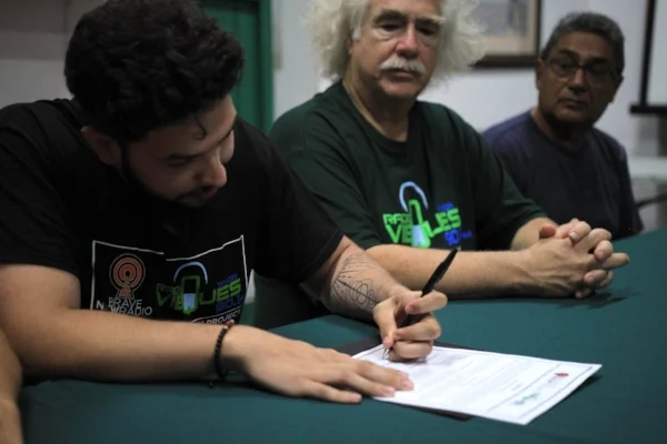 Station Manager Sebastian Escobar signing the Sister-Station Contract Agreement. Rob Rabin (Center) and Armando Torres-Sanes (Right) look on. 