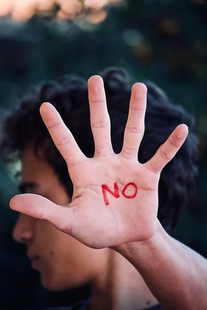 A person, turned away from the camera and holding their hand up with the word "no" written on their hand.