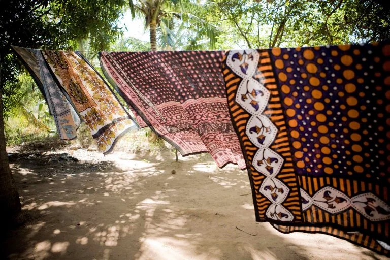The sun streams through sheets hanging in a village.
