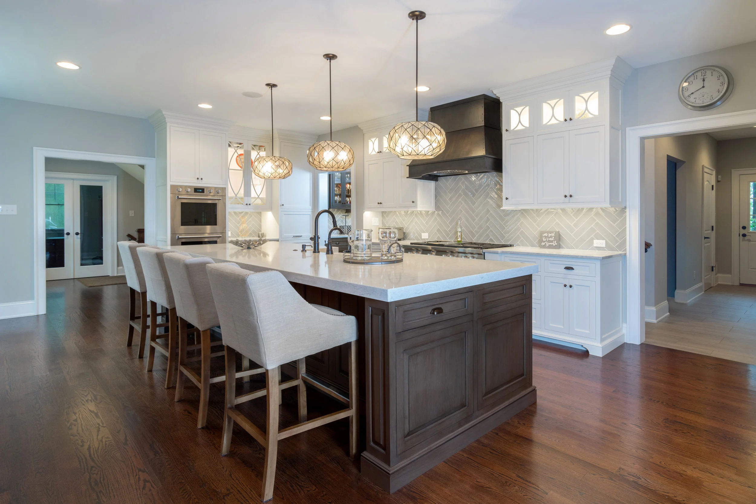 This view of the kitchen shows off the stain and glaze cherry island and painted white perimeter cabinetry. The custom metal hood with gray subway tile and fun exciting lighting keeps your eye moving throughout the space.