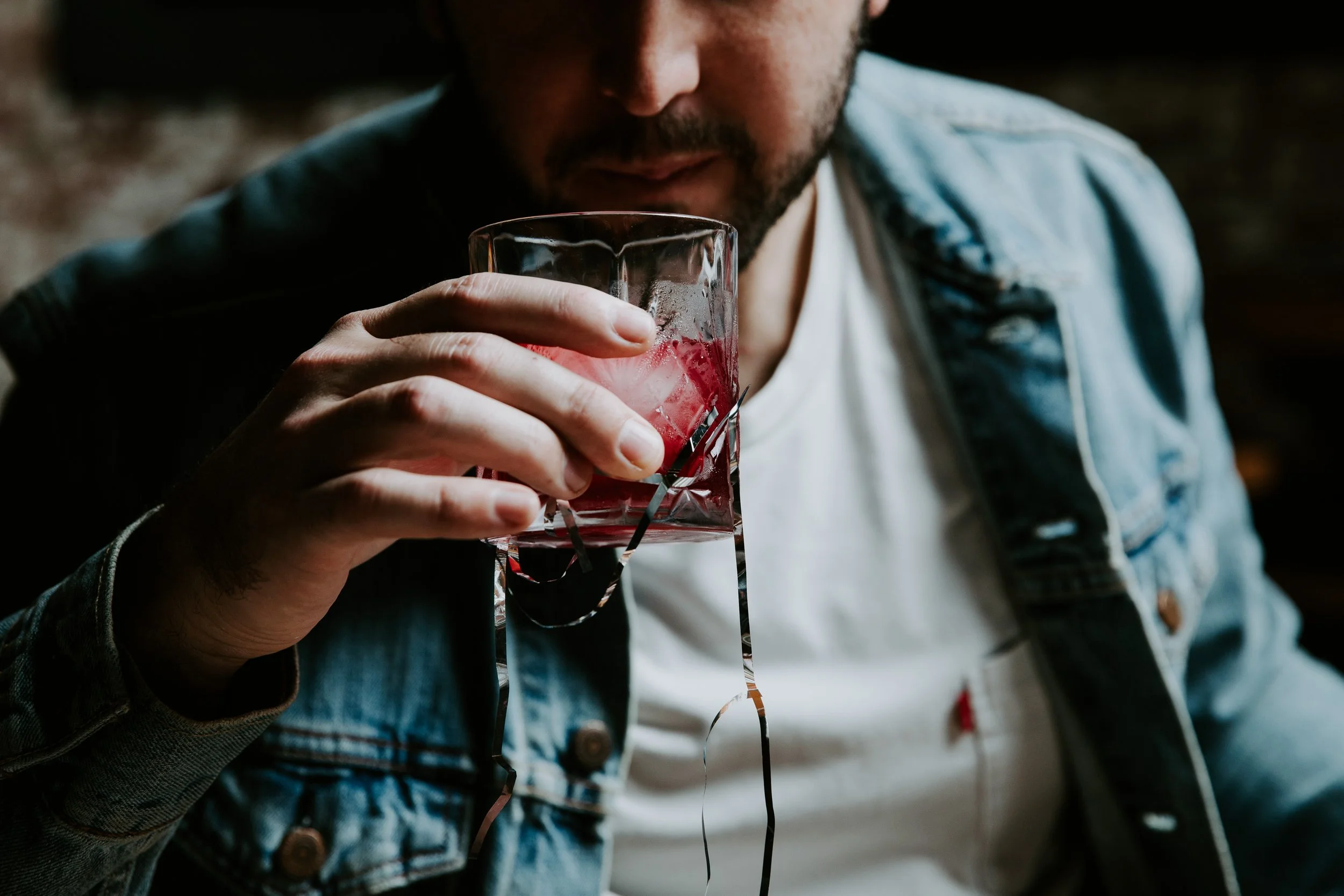 Man wearing a denim jacket sipping a red cocktail with ice from a glass at Bhang Brunswick, Melbourne.