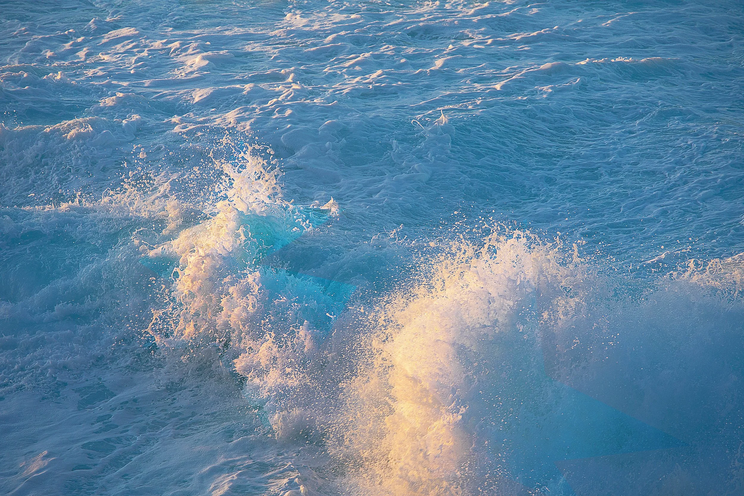Ocean waves with foam, illuminated by sunlight, creating a blue and white textured seascape.