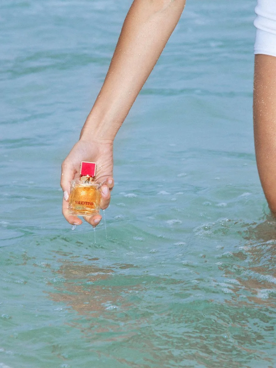 A person holding a Valentino perfume bottle in the ocean water.