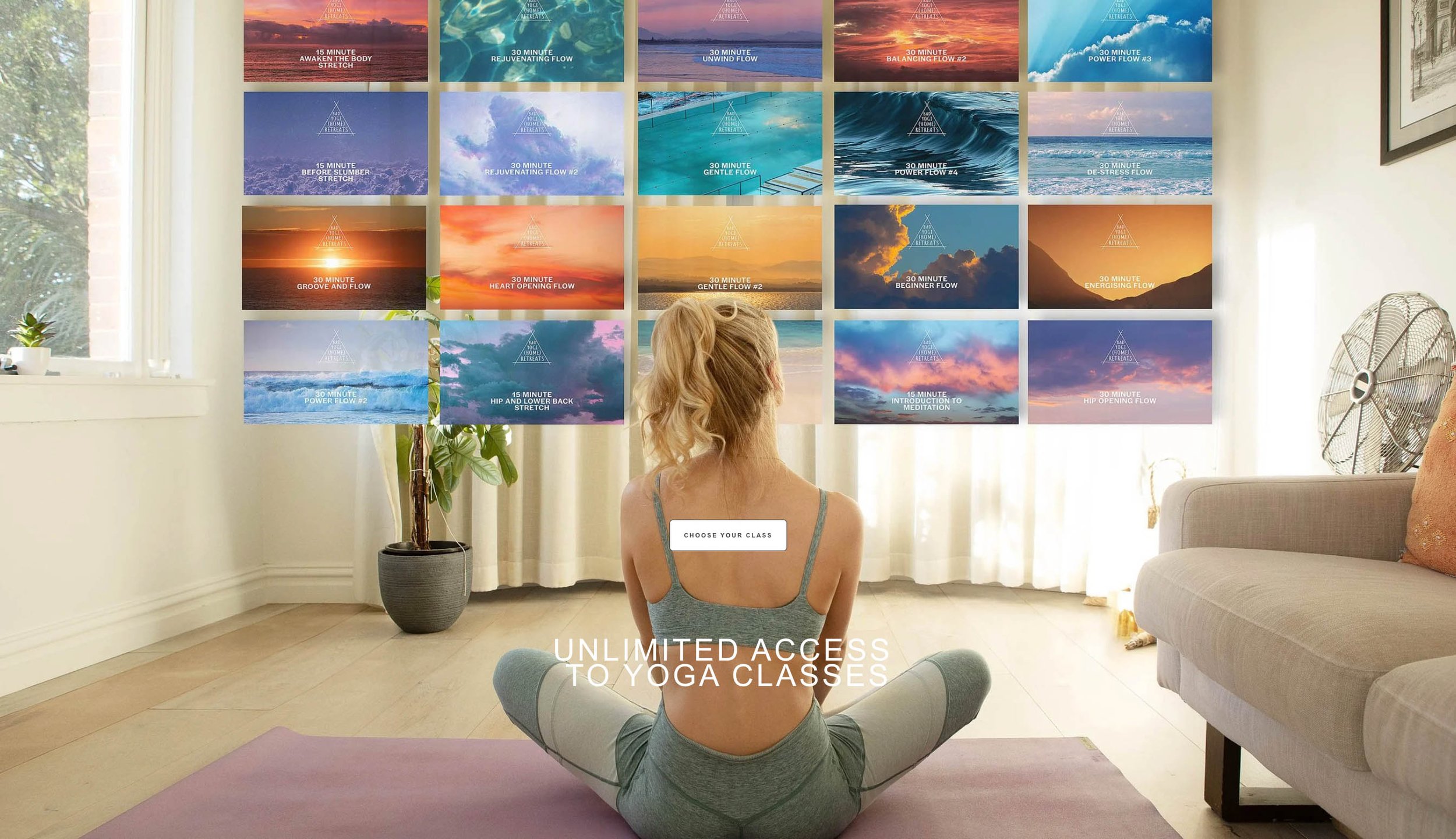 A woman practicing yoga indoors in front of a wall with colorful posters of various yoga classes, with sunlight coming through a window and a large fan on the right side.