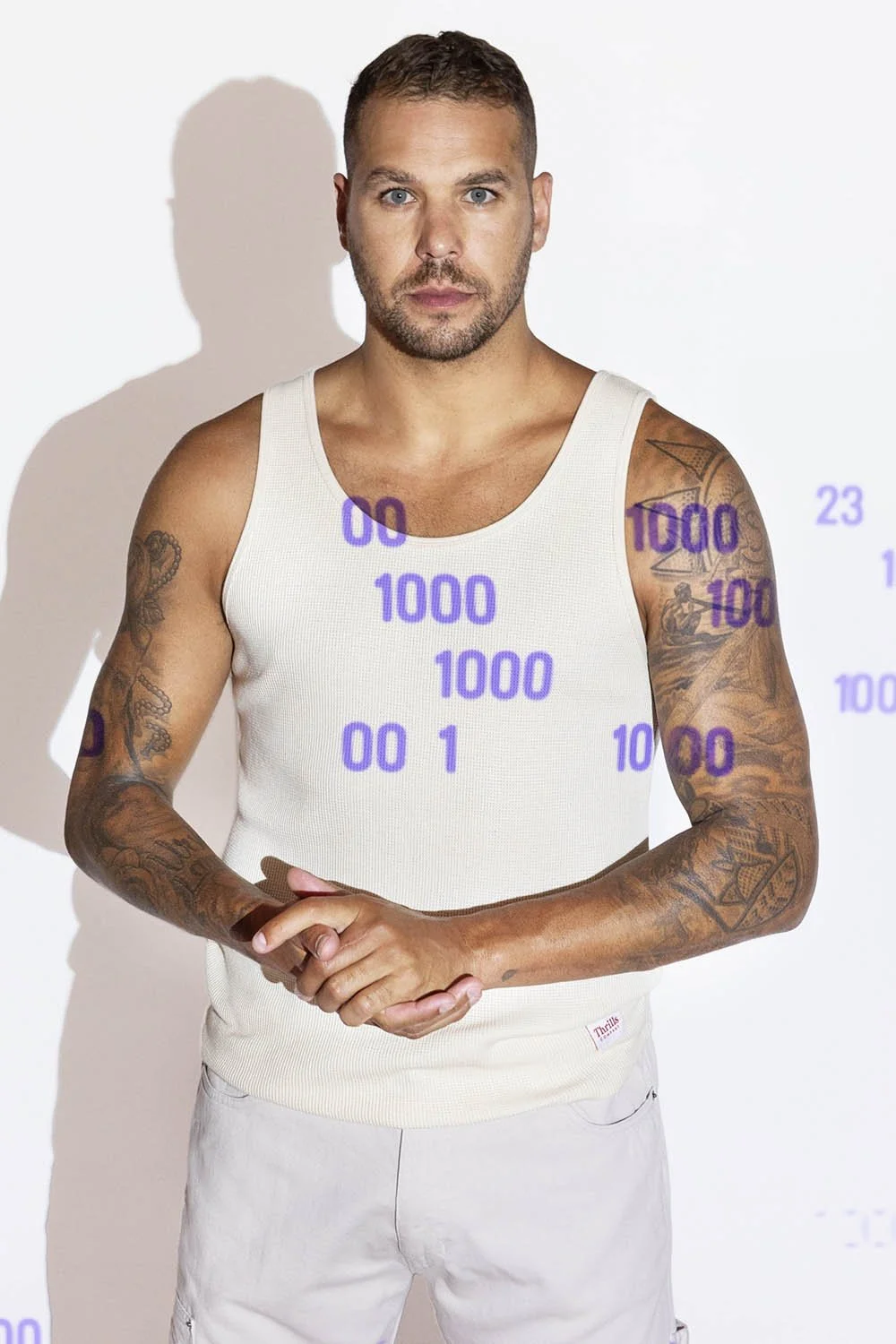 A man with short brown hair and tattoos on both arms wearing a white tank top standing against a white background with purple numbers and symbols projected or printed onto him.