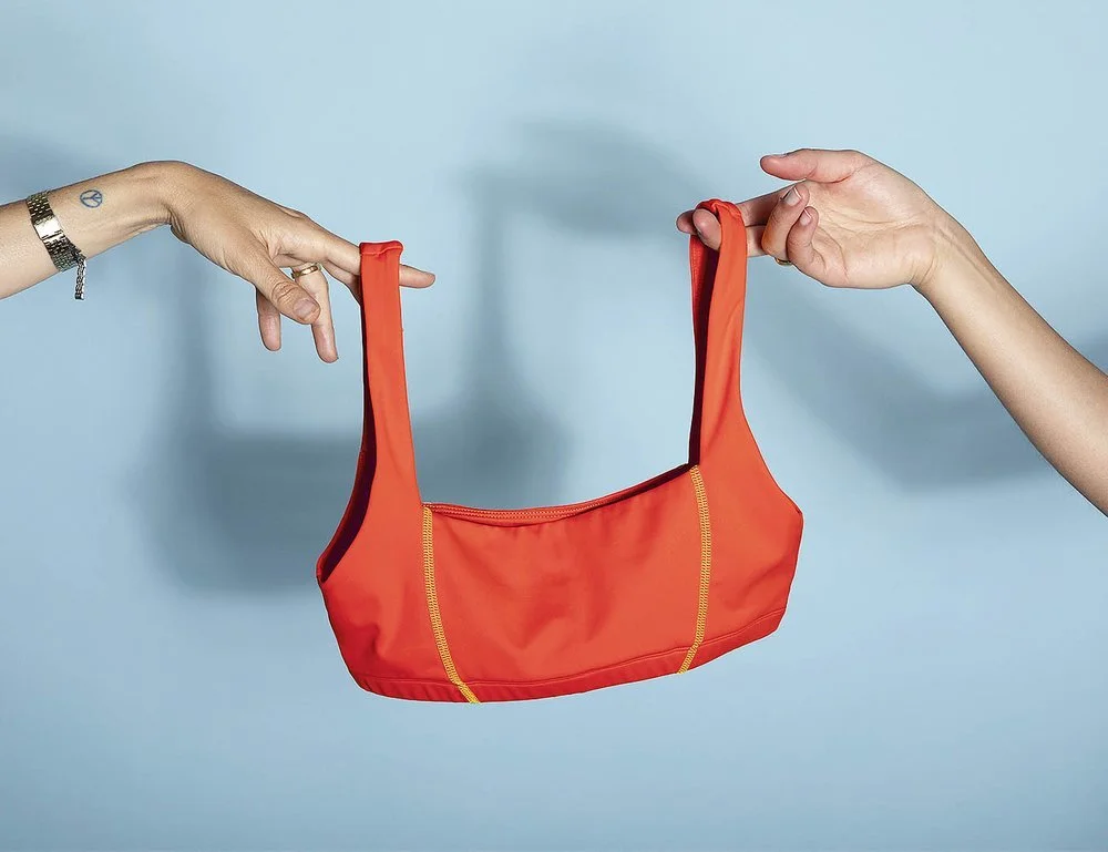 Two hands holding a red sports bra against a light blue background.