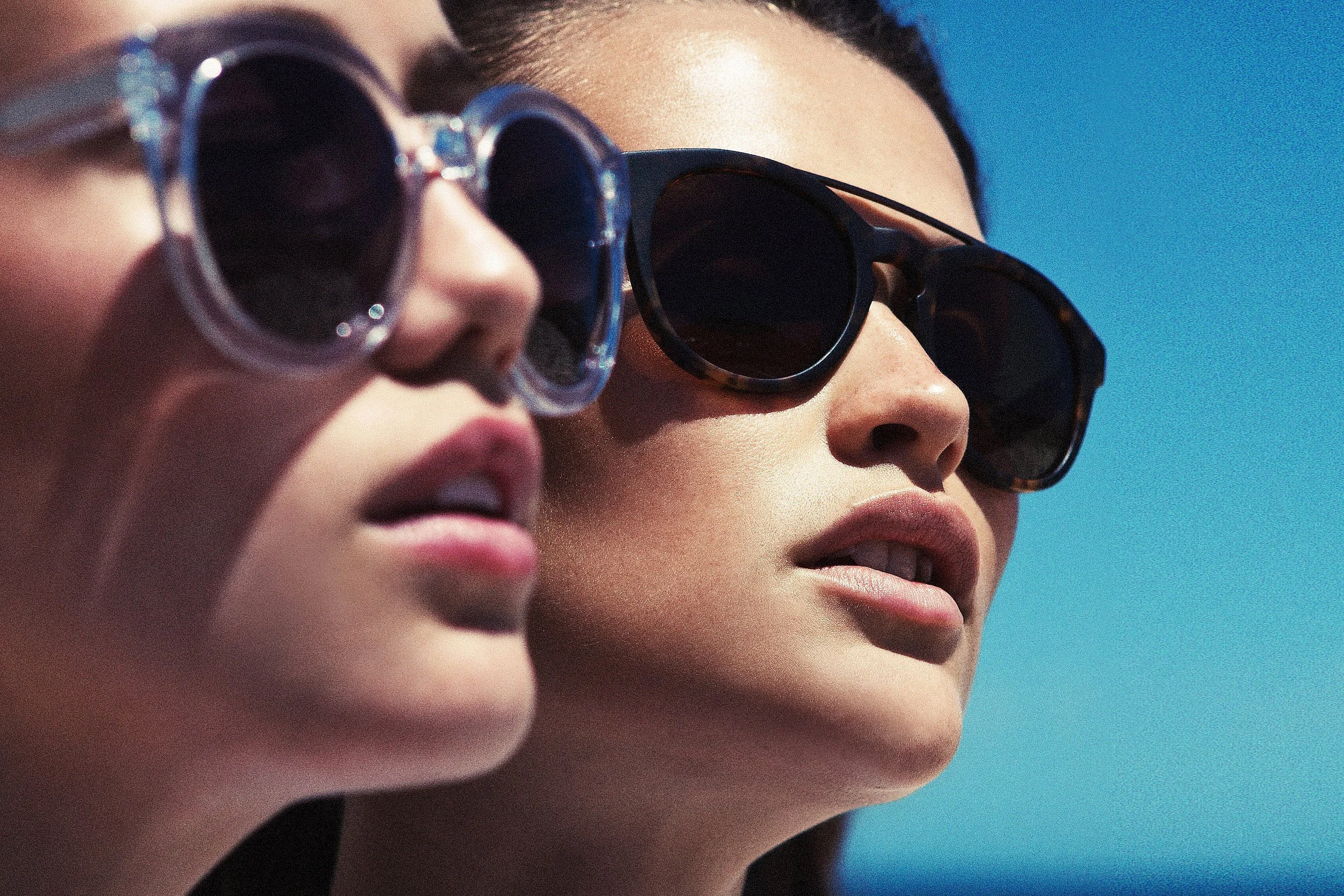 Close-up of two women wearing sunglasses, with blue sky in the background.