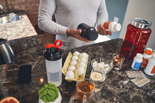 Photo showing athletic man examining sports nutrition products by a kitchen surface