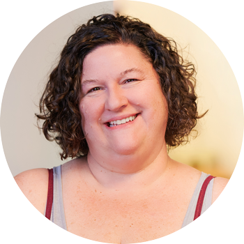 A woman with curly brown hair smiling at the camera in front of a light-colored background.