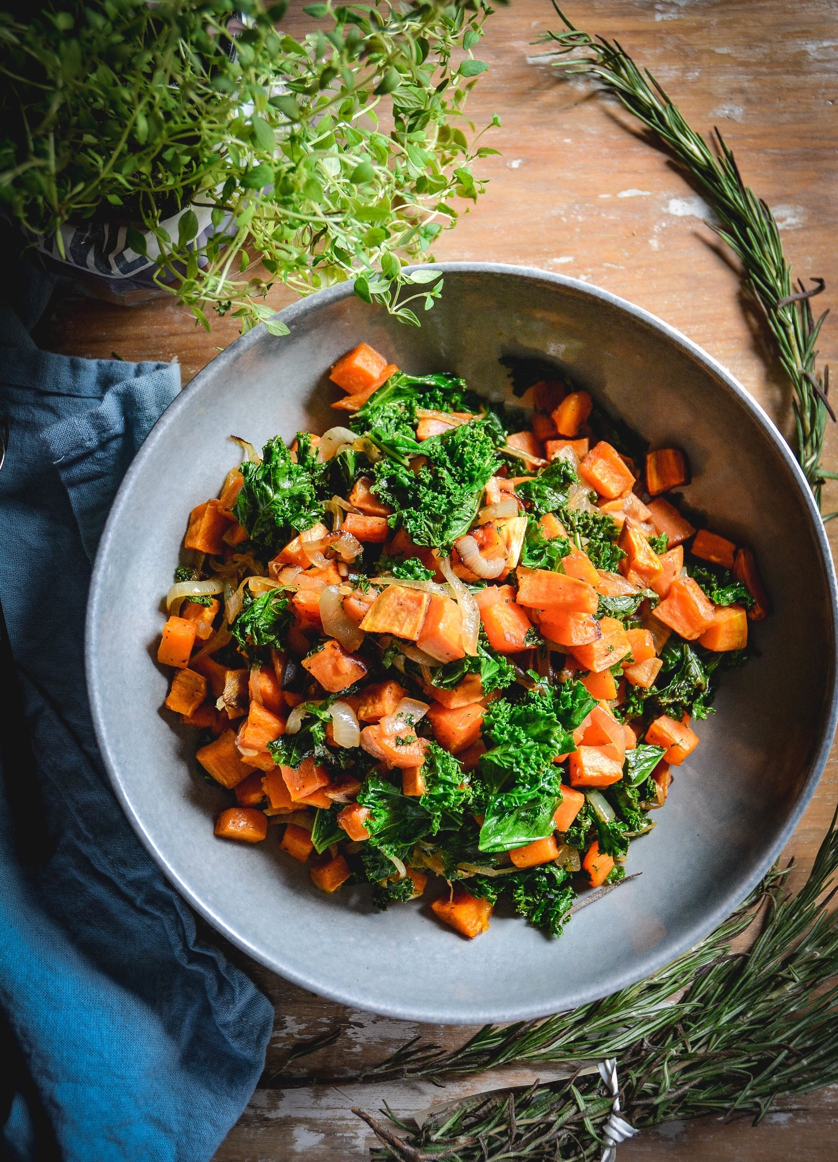 sweet potatoes with kale in large bowl on table with thyme and rosemary