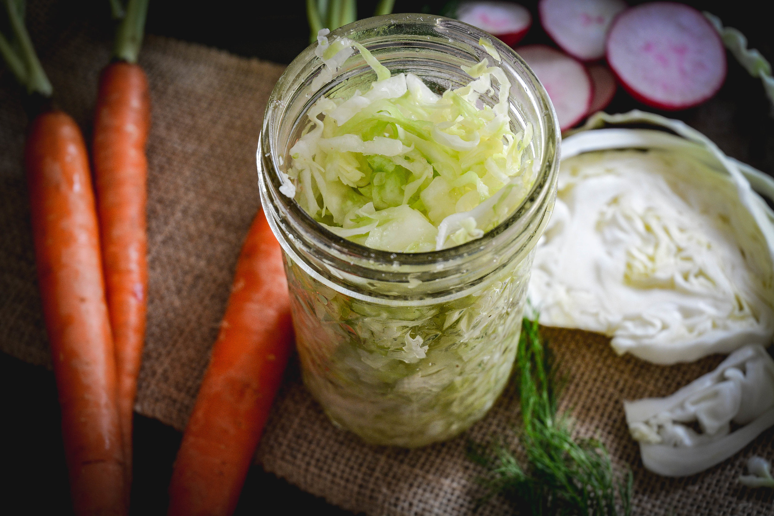 Sauerkraut in jar next to carrots, cabbage and radishes