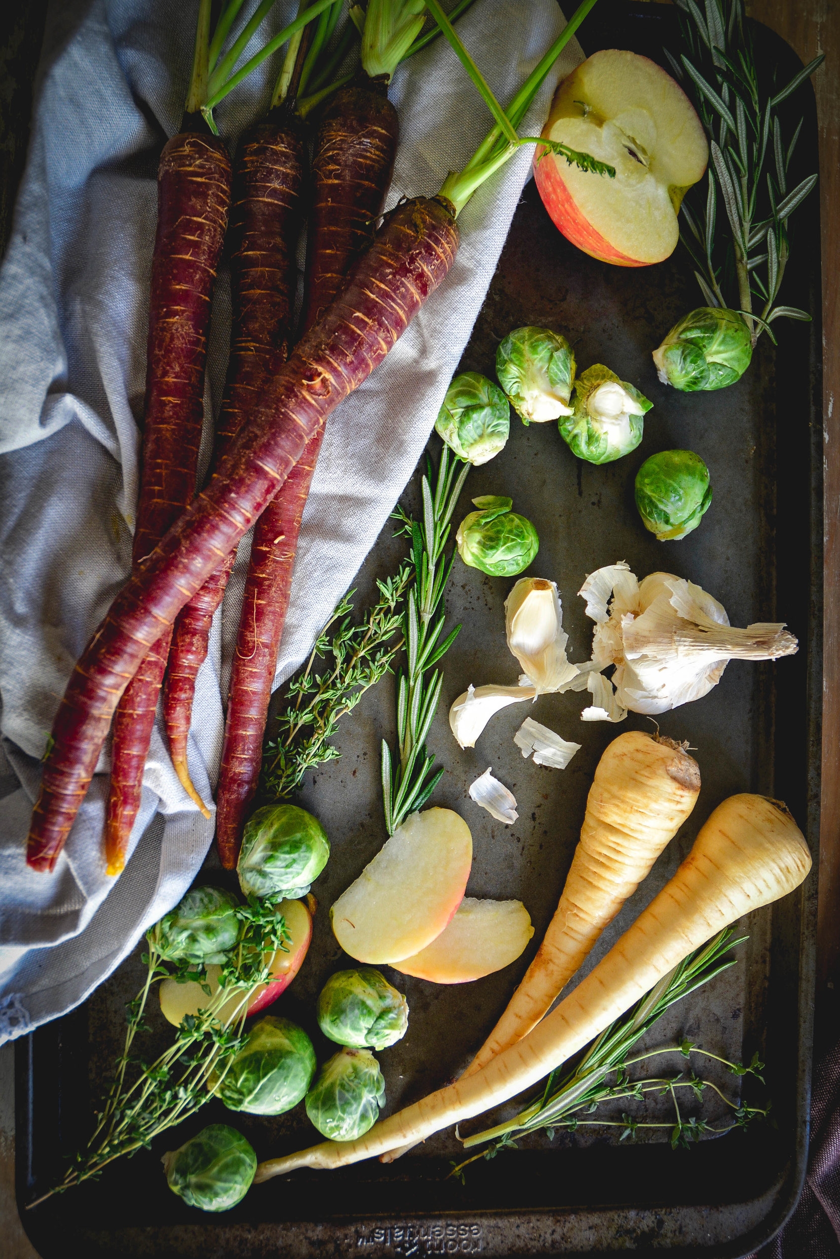 carrots, brussels sprouts, apple, parsnip on tray with herbs and napkin