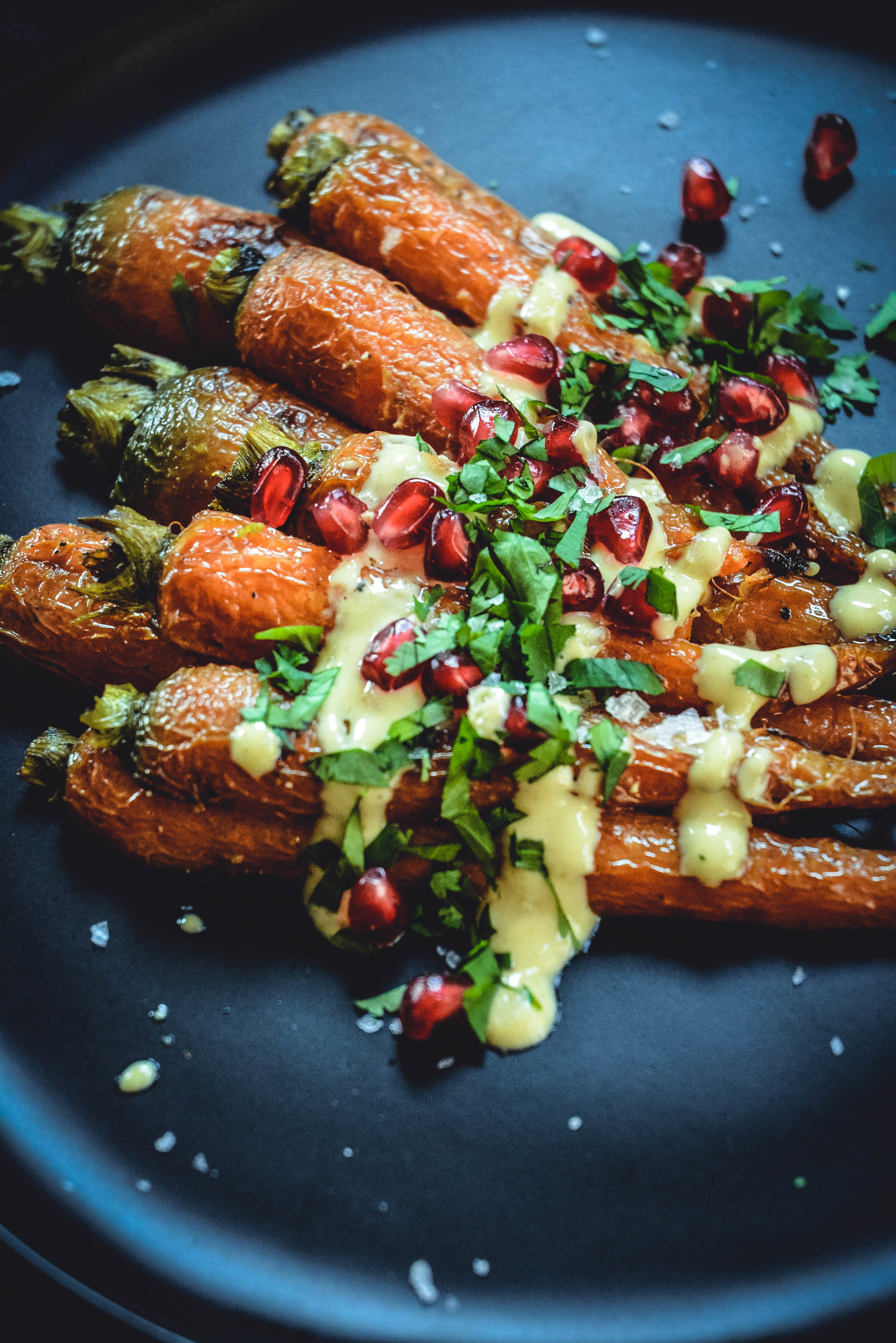 Roasted Carrots With A Simple Orange Tahini Sauce And Pomegranate on black plate - side view