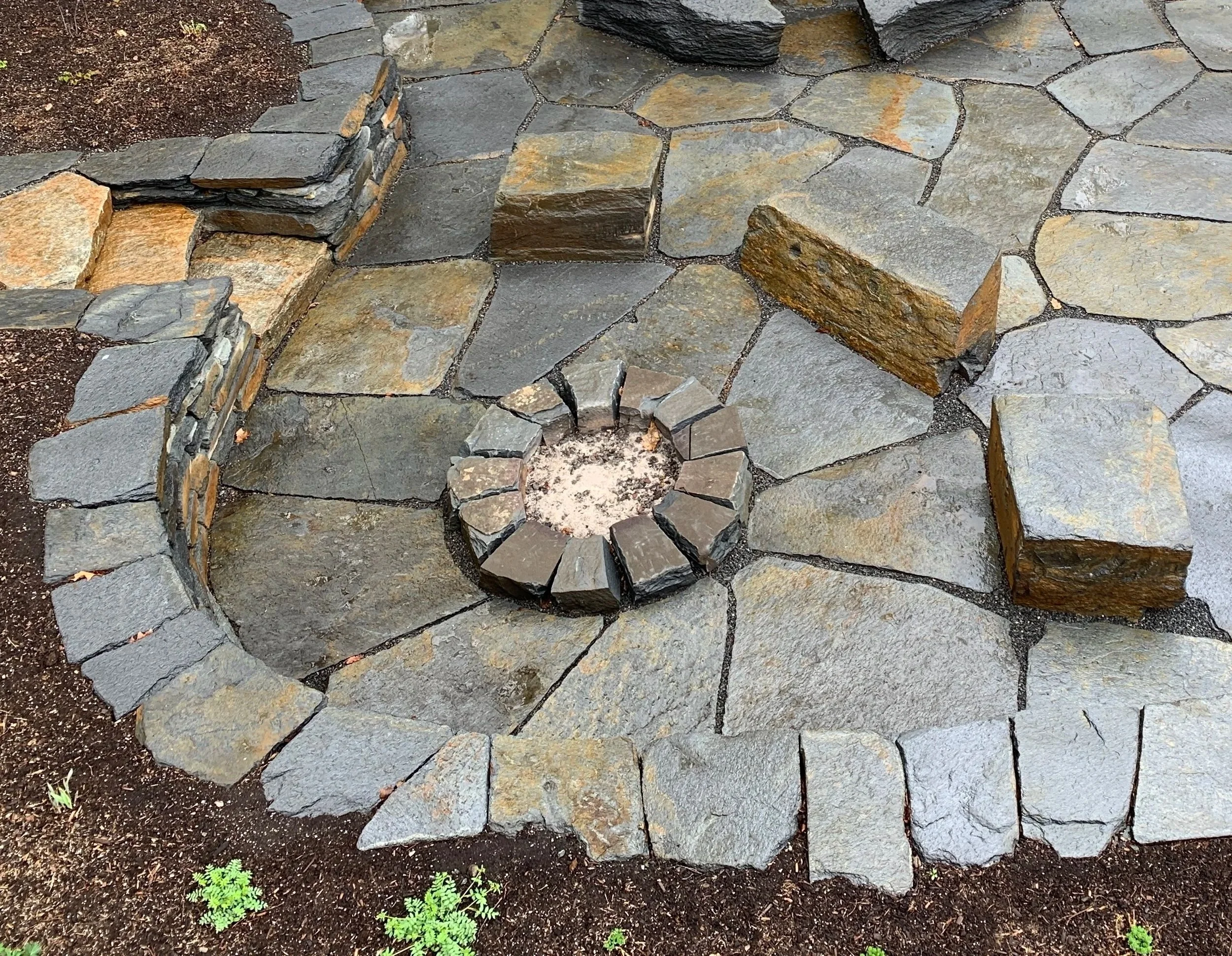 Hand split granite fire pit surrounded by stone benches and stone walls