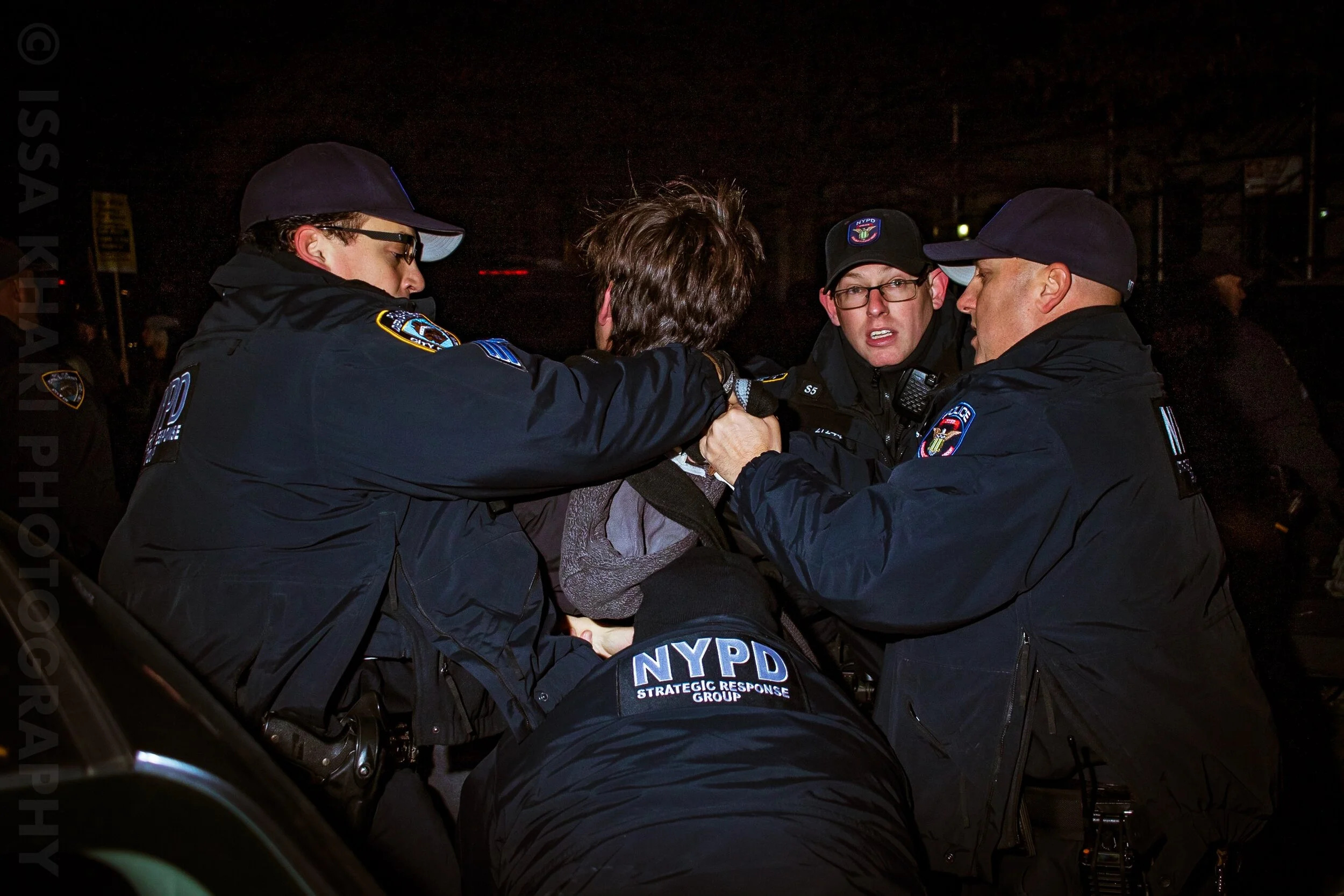 Several NYPD officers detaining and struggling with a person during a nighttime protest or altercation.