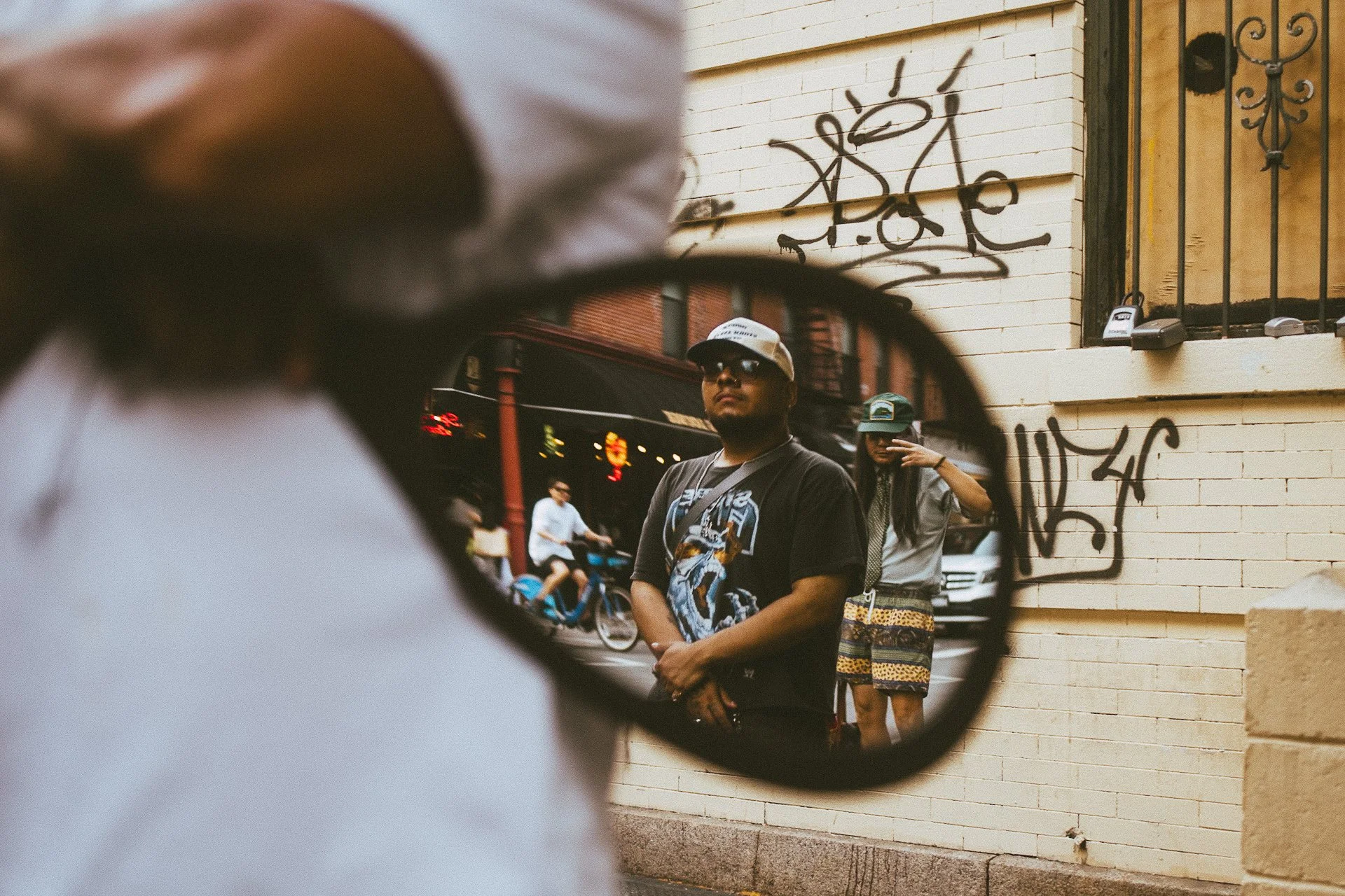People standing in front of a building with graffiti, reflected in a convex mirror.