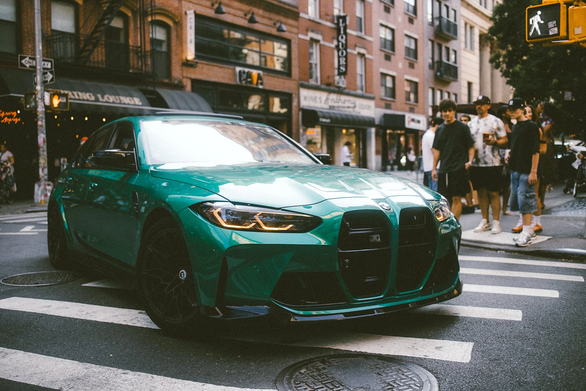 A vibrant green sports car, likely a BMW, parked on a city street with buildings and pedestrians visible in the background.