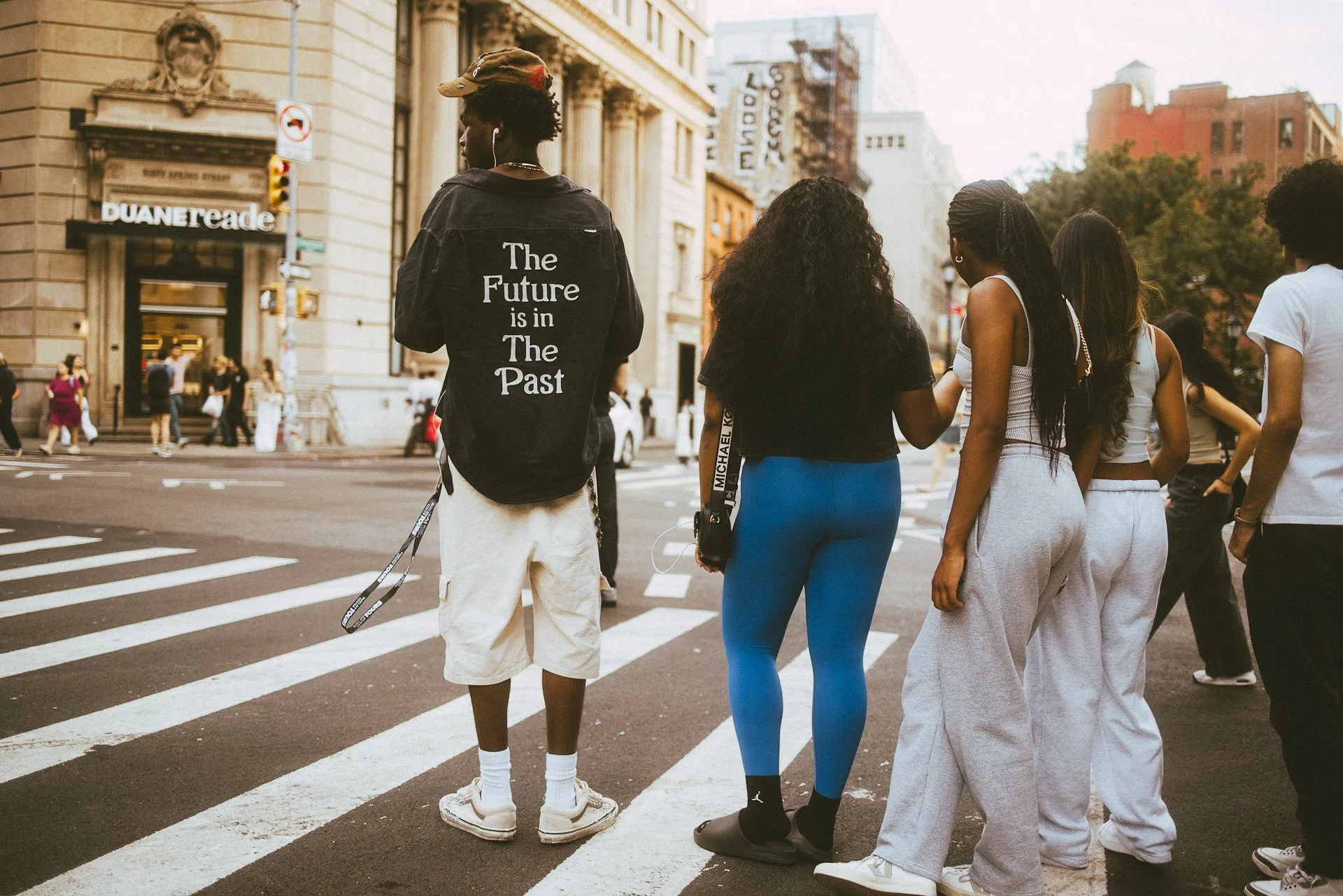 A group of diverse young people waiting to cross a city street at a crosswalk.
