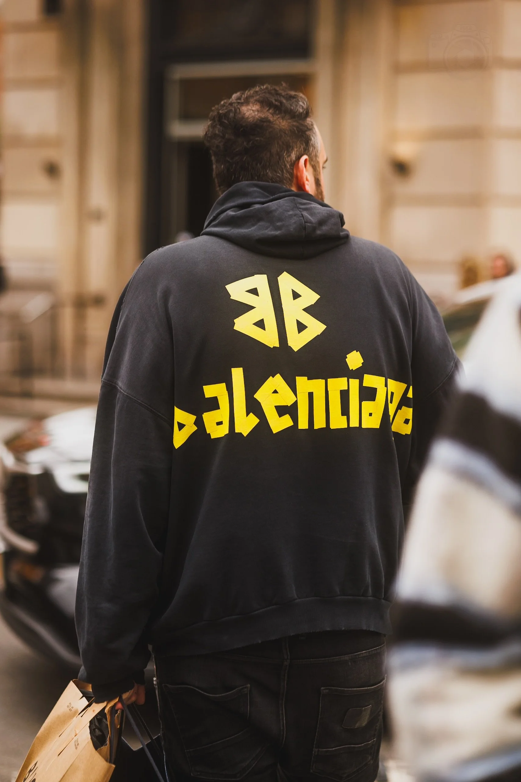 Person with dark hair and beard wearing a black hoodie with yellow stylized text on the back, shopping in a store.