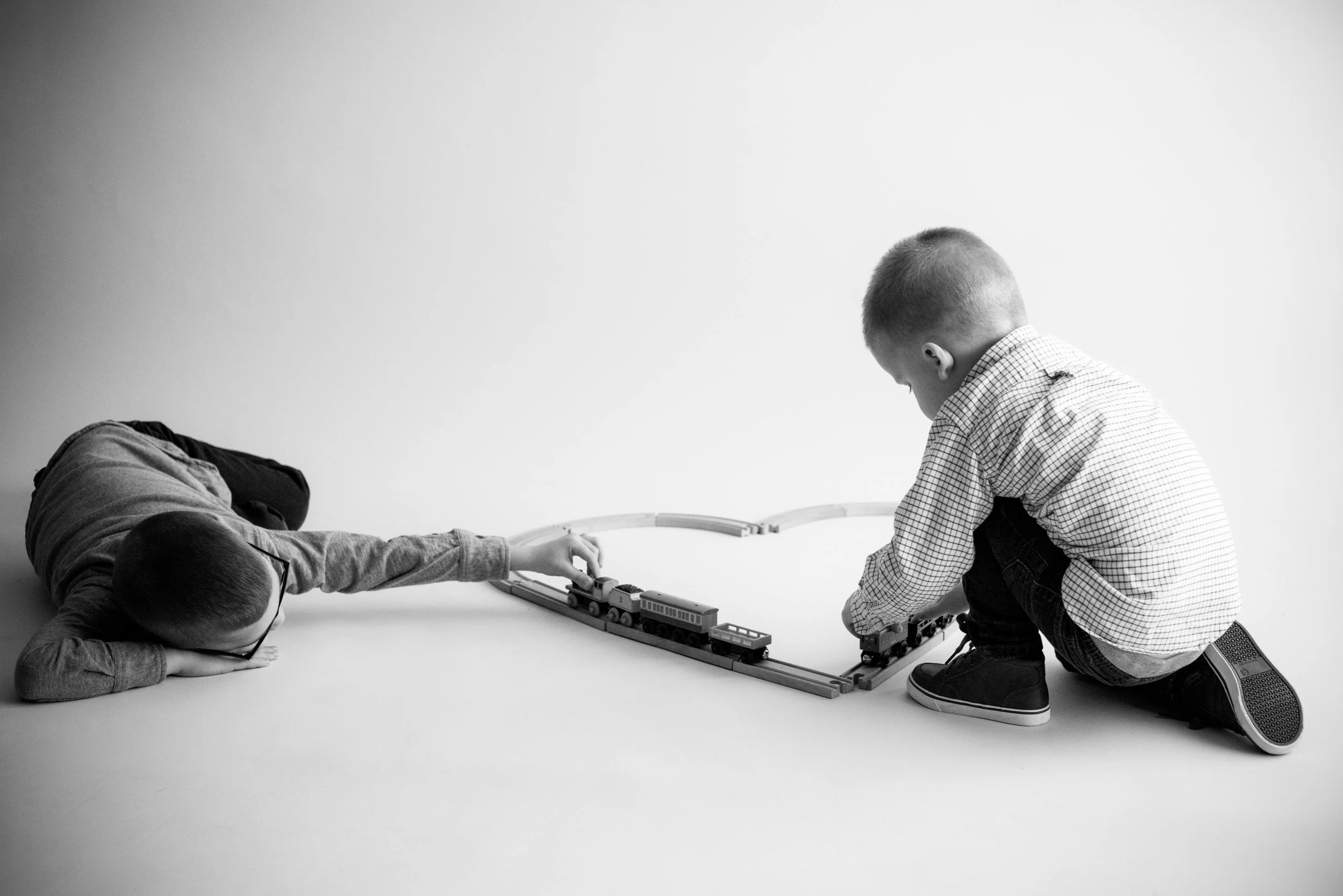 Two boy children playing with toy trains during photo session in Cedar Rapids, Iowa in black and white. 