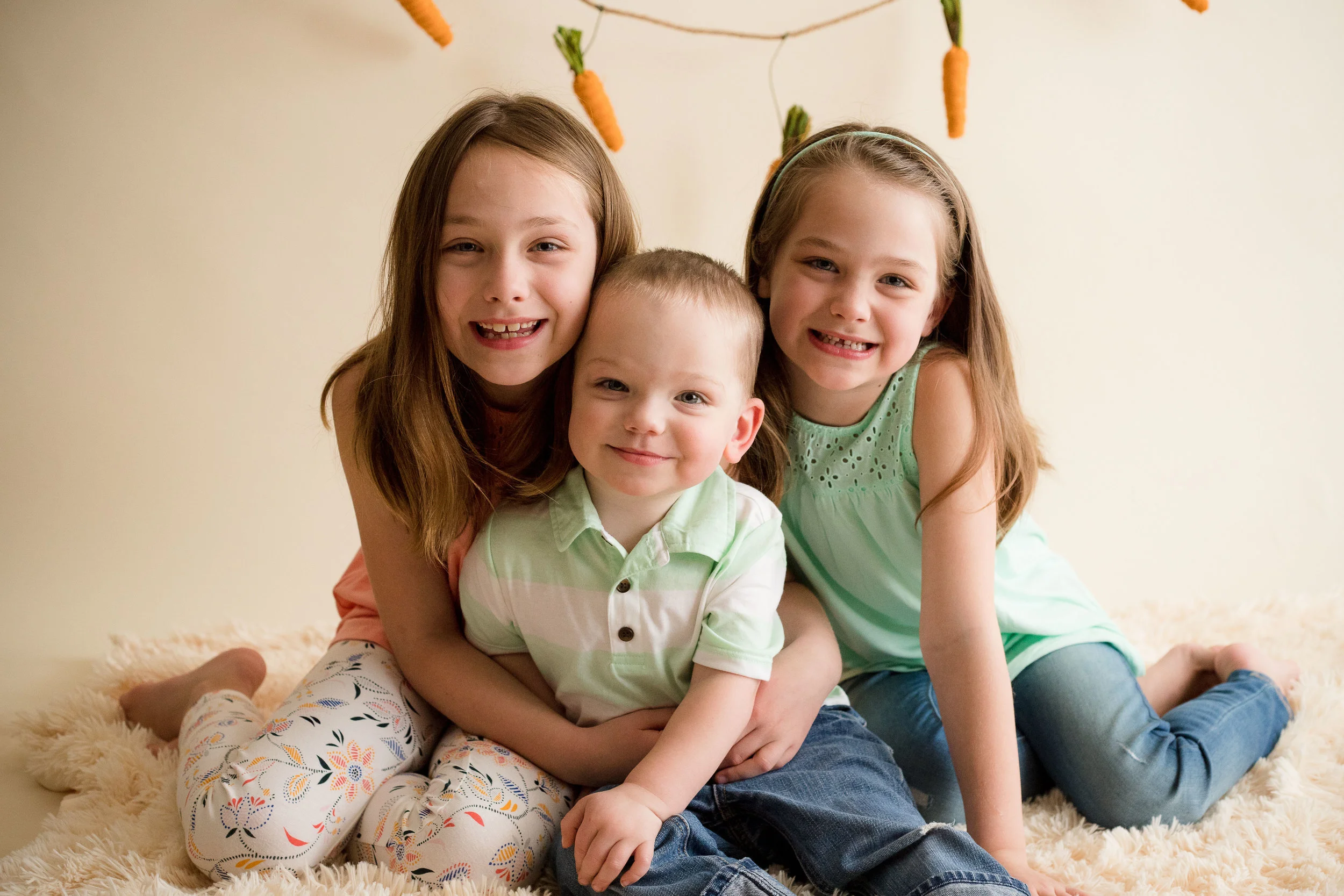 Two sisters and their little brother sitting and smiling in a photo during Easter Mini Session. 