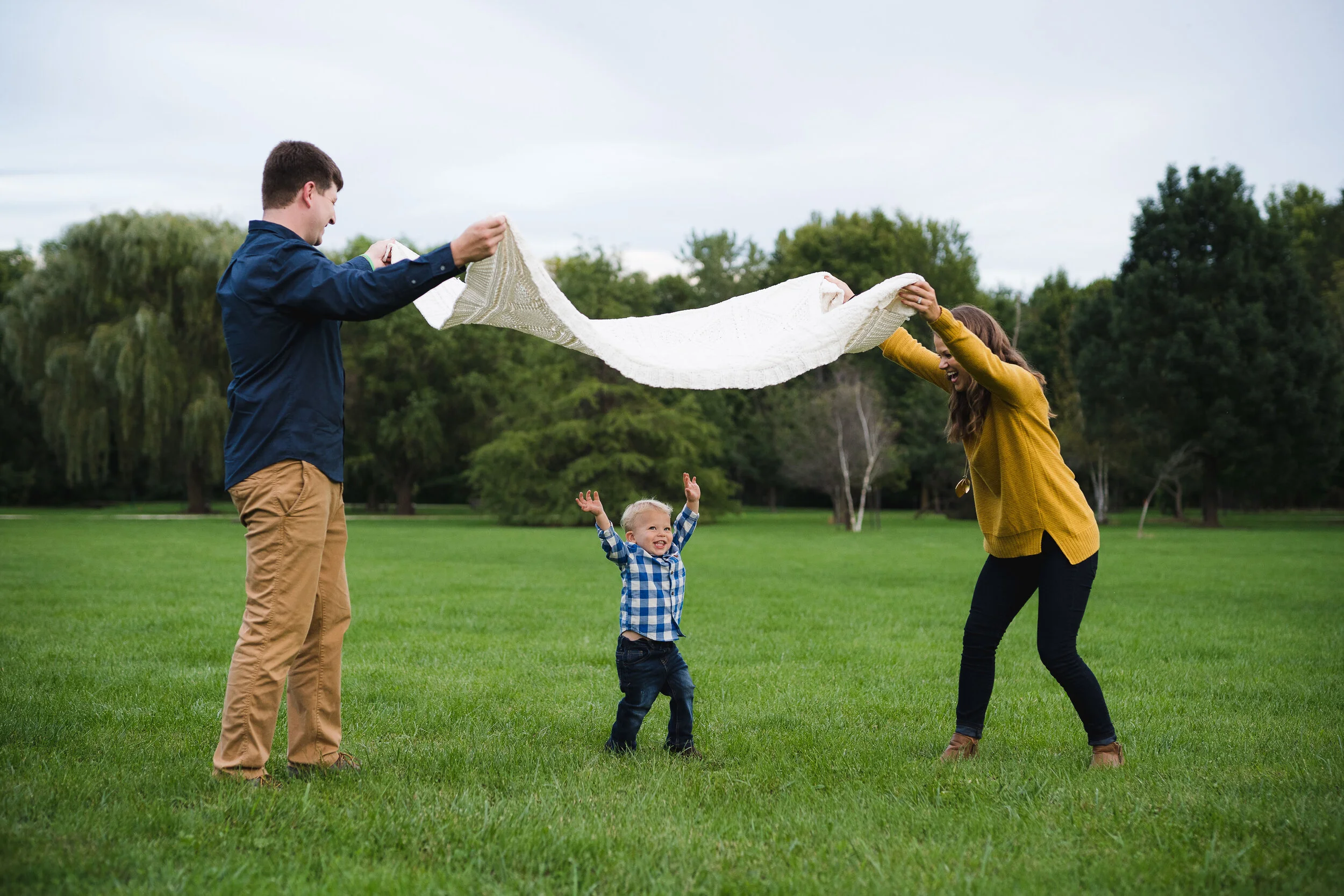 A family of three playing in a park during a fall photo session in Cedar Rapids, Iowa.