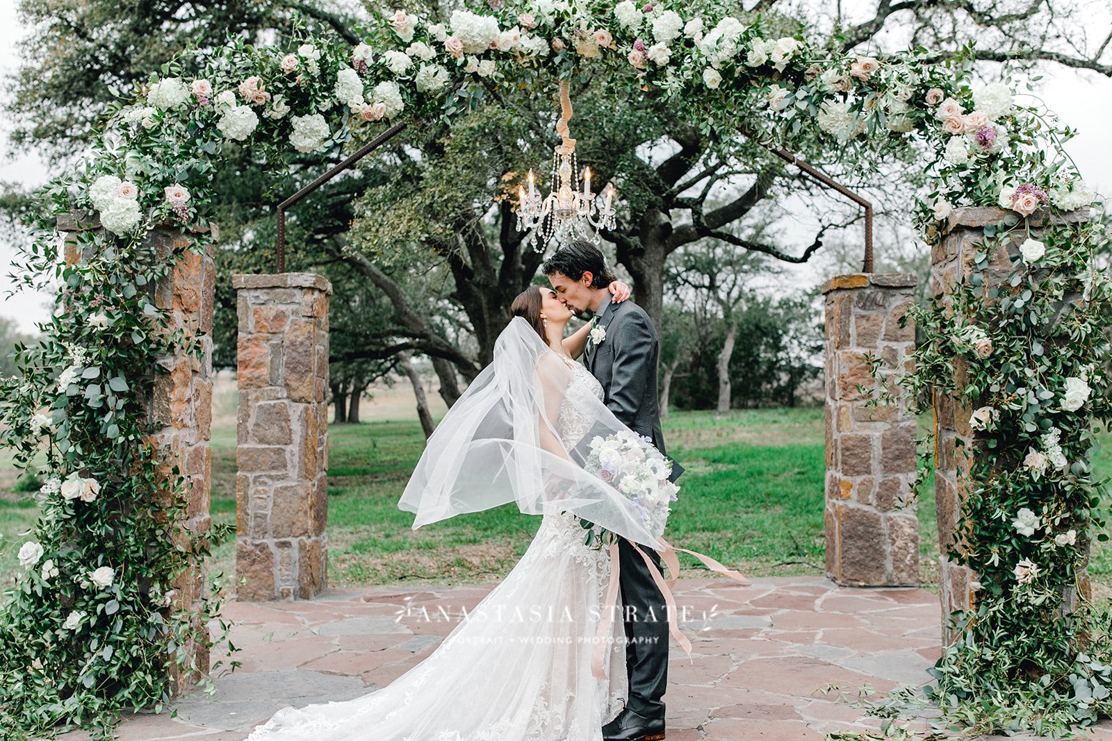 bride and groom kiss under the greenery wedding arch