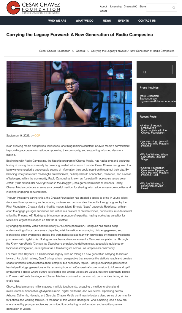 Young man with glasses sitting at a desk in a dark room with a computer, microphone, and a background featuring shelves with books and decorative objects, illuminated by blue lighting.