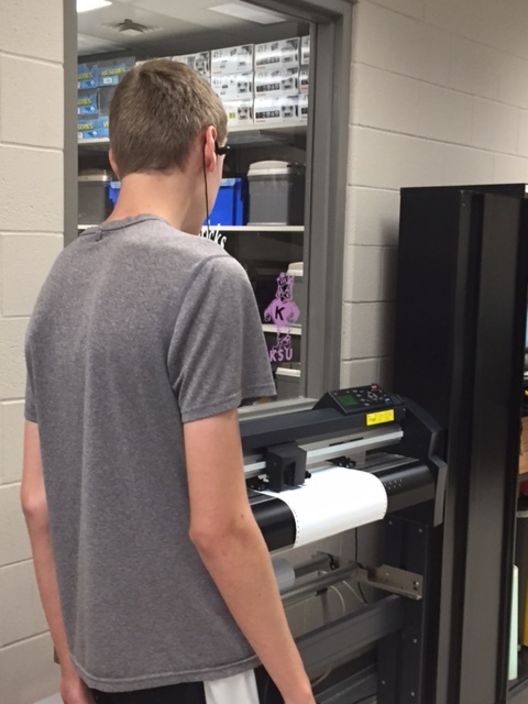 Graphic Design student watches his project finish on a vinyl-cutting printer.