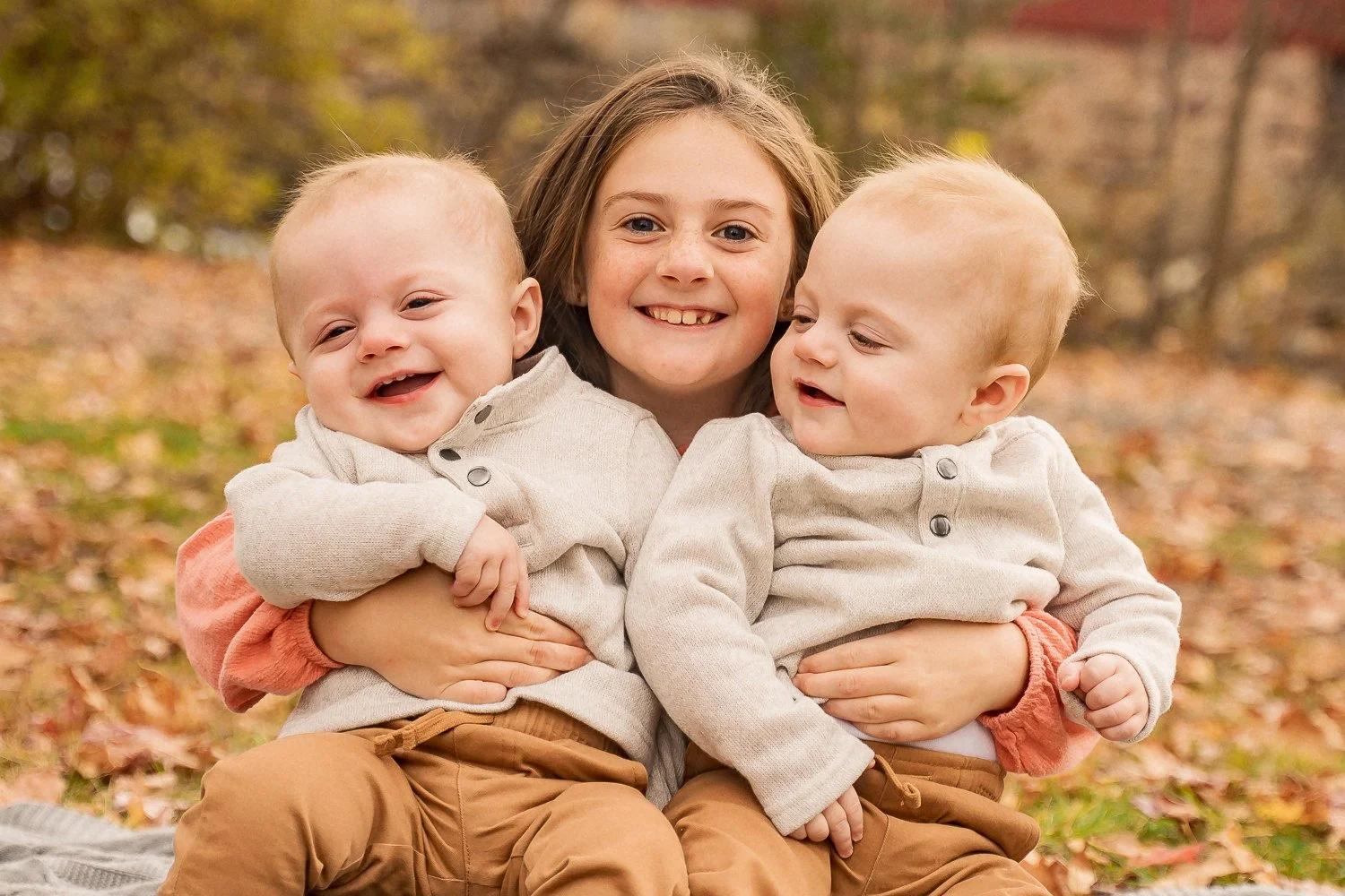 14-teresa-mansbach-older-sister-holding-smiling-twin-babies-outdoors-id-158.jpg