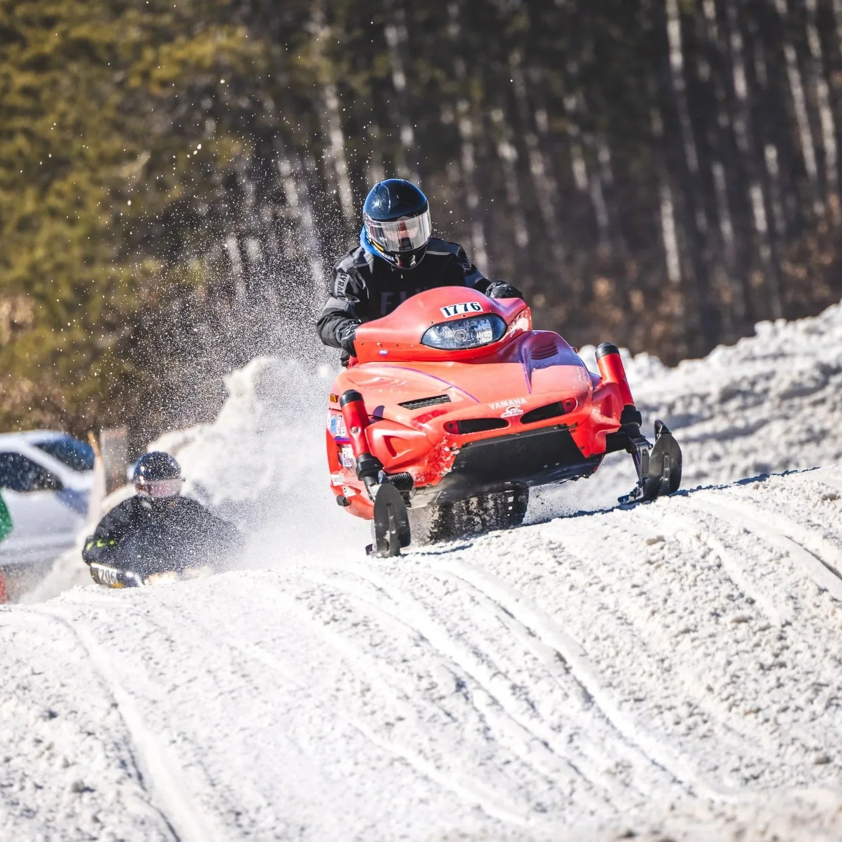 A person riding a red snowmobile on a snowy trail with trees in the background, during daytime.