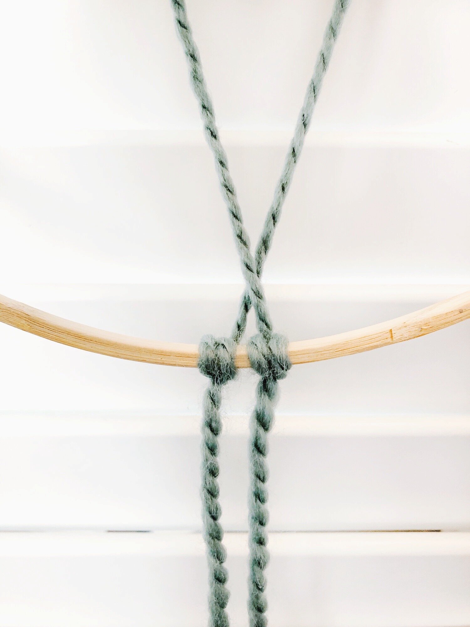  Starting with the outermost strand, bring it behind the other strands and behind the ring. Attach it with a double half hitch knot. Keep it centered as much as possible. 