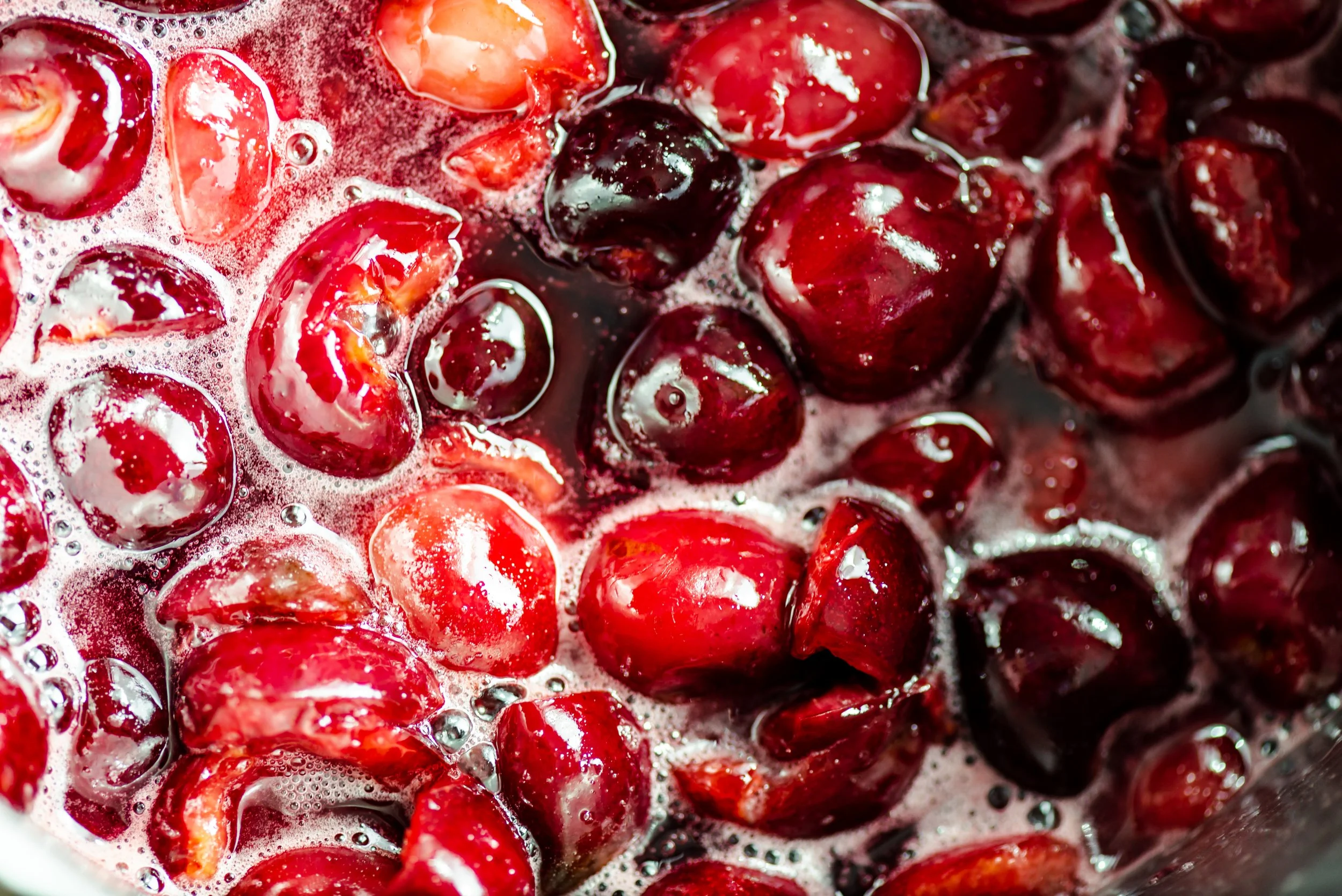Close-up of fresh cherries being cooked, with some cherries cut open and bubbling in liquid.