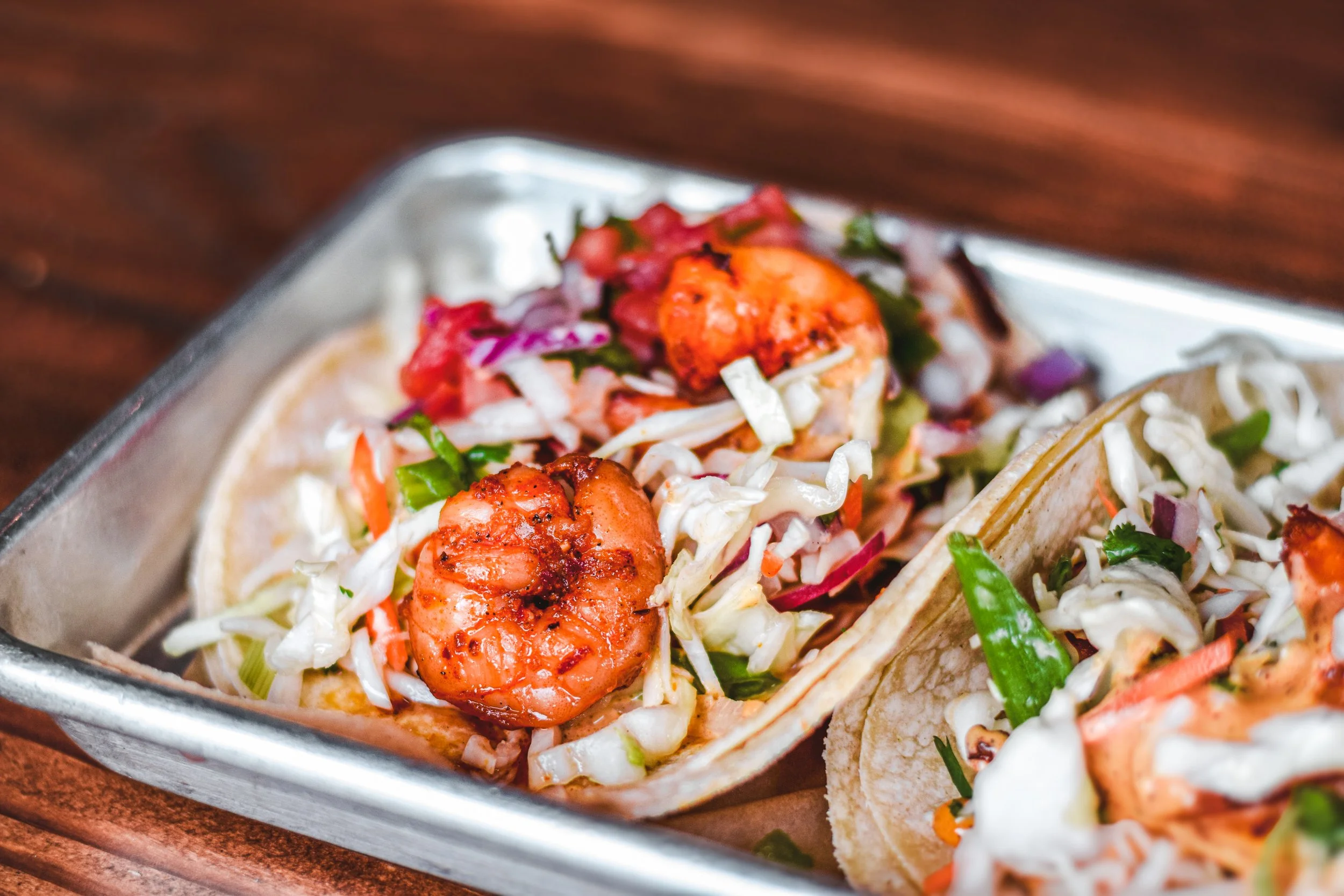 Shrimp tacos topped with cabbage and salsa in a metal tray.